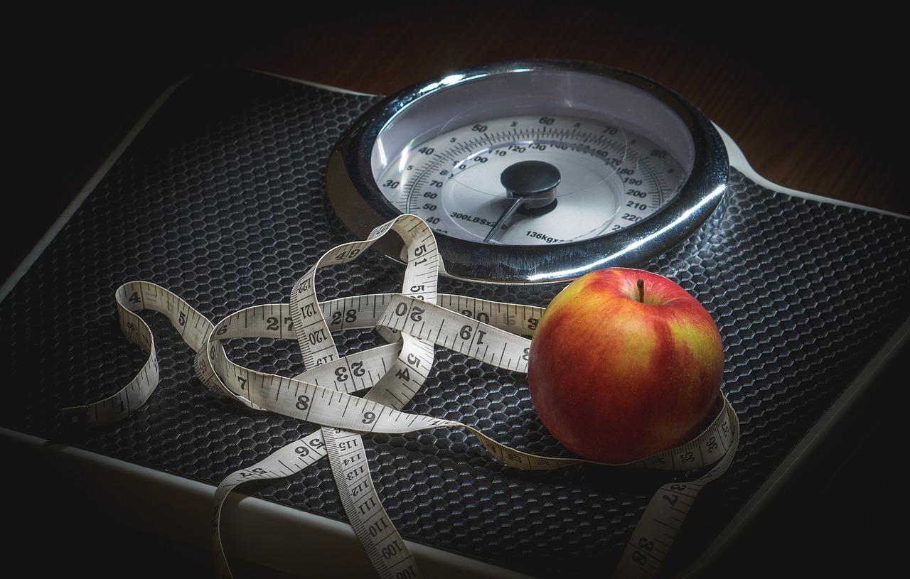 A set of scales with a tape measure and an apple on top. Healthy weight loss is very achievable with a balanced diet and exercise.