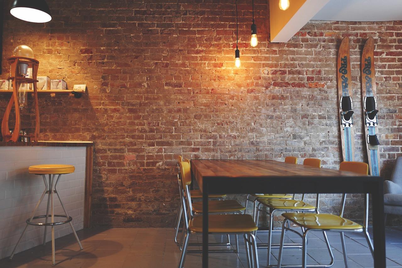 The interior of what looks to be a cafe or restaurant, with a large table and chairs, as well as a stool next to a countertop. Wooden skis are hanging up. Some workplaces offer Portuguese classes.
