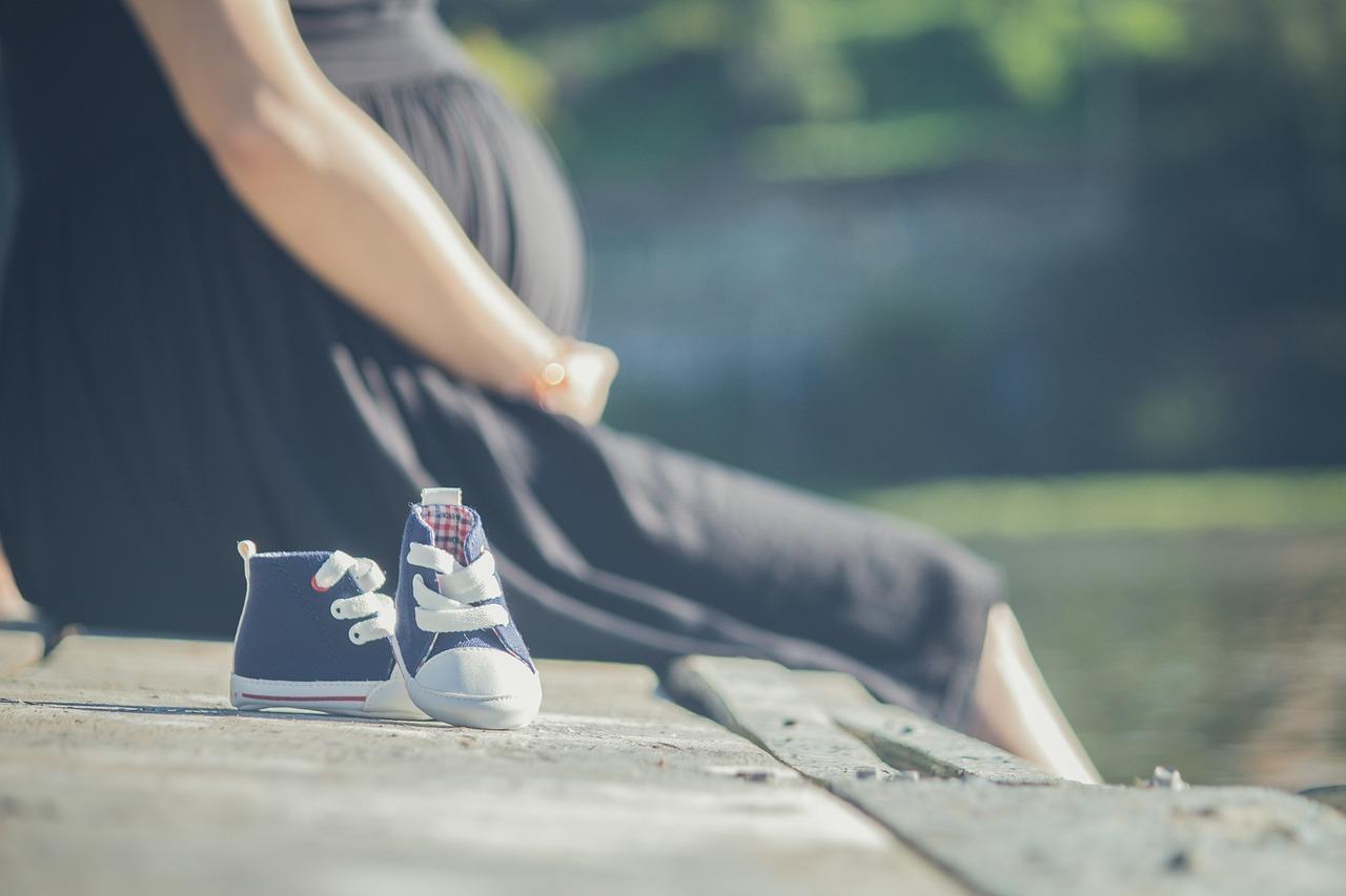 Pregnant woman in a black dress sitting on a bench with blue baby's shoes next to her. A good pregnancy diet is very important.