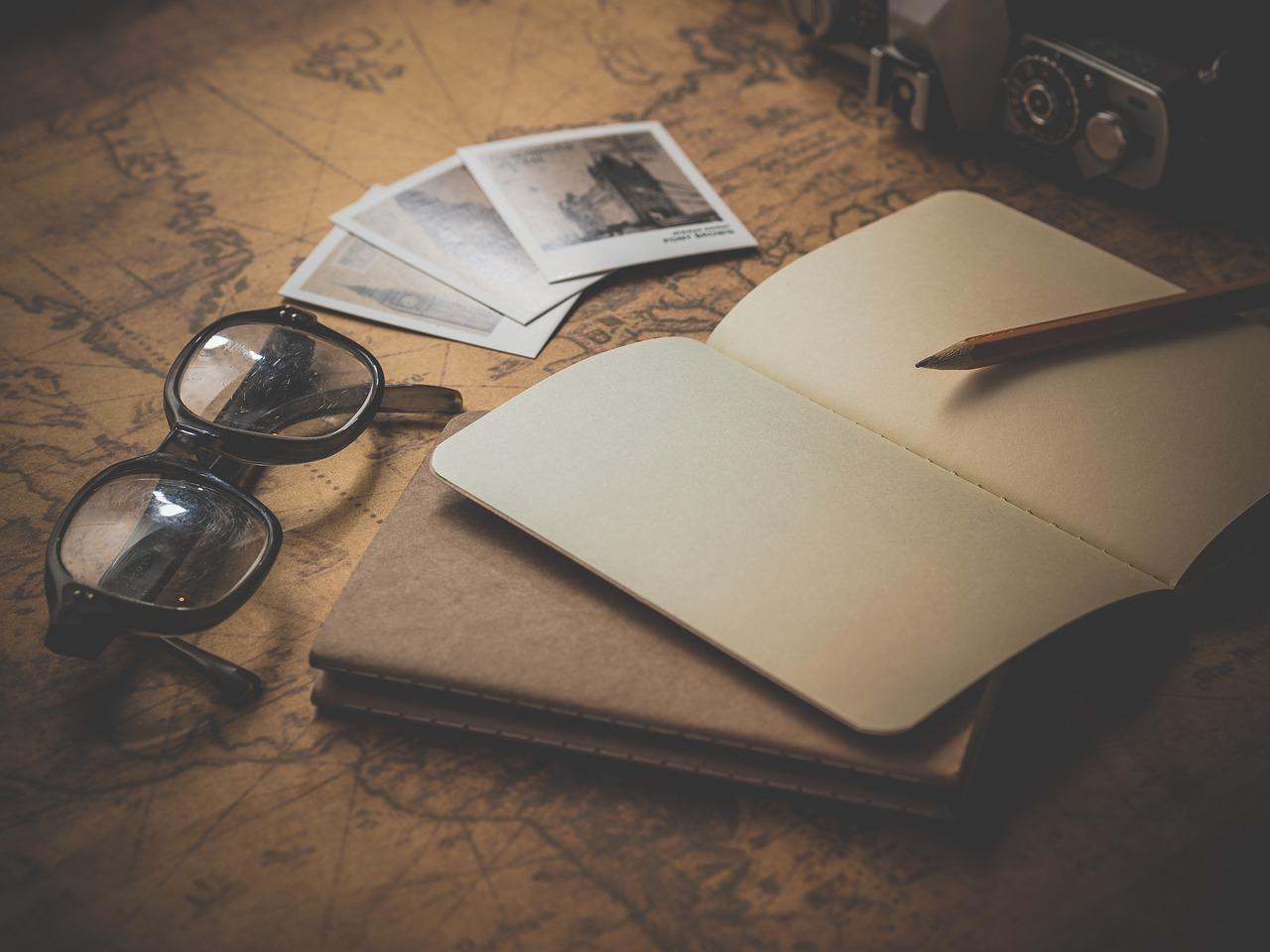 A retro-styled image consisting of a pair of glasses, polaroid photos, notepads and a pencil on top of a map. There are many reasons to take Portuguese lessons.