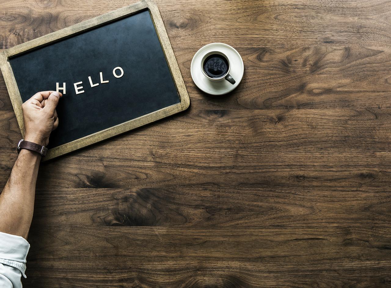 An image of a hand placing the word "hello" onto a black chalkboard with a cup of coffee next to the chalkboard. Learning the letters in the Portuguese alphabet is an important task if you want to learn Portuguese.