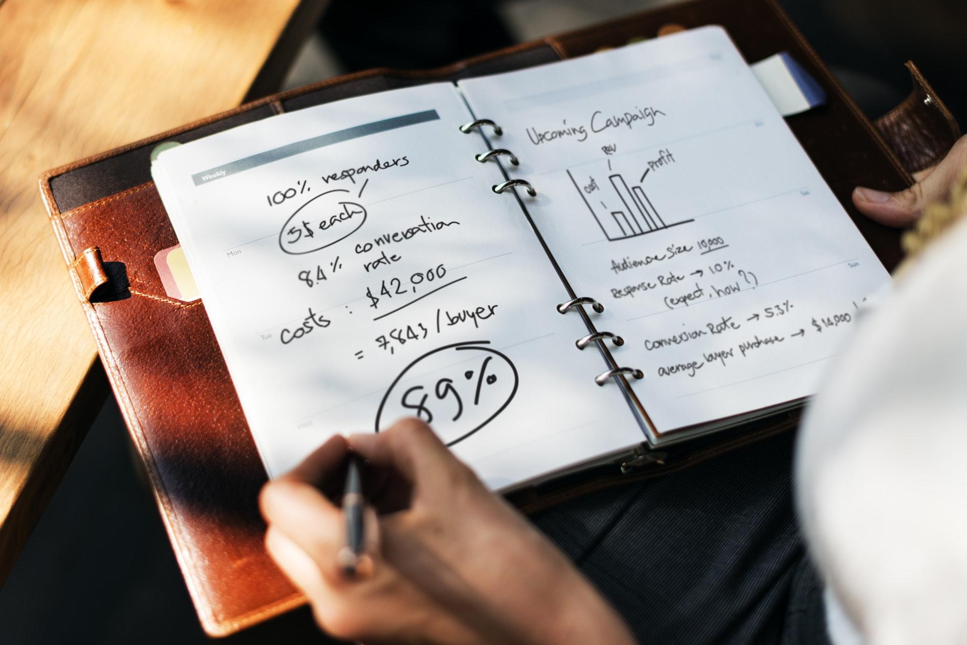 a person using a black felt-tipped pen to write and draw graphs in a leather-bound notebook