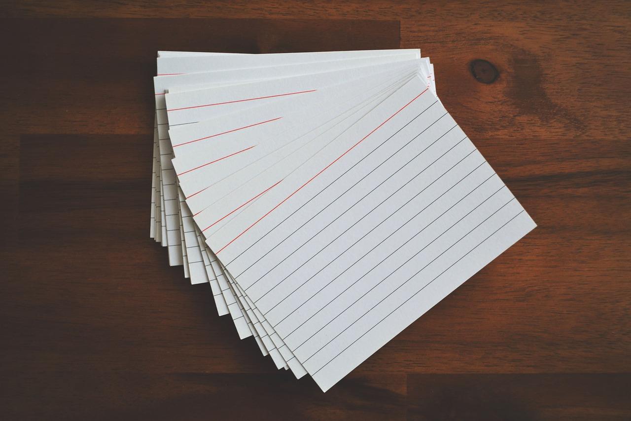 An image of a pile of flashcards on top of a wooden surface. Using flashcards can help you memorise the Portuguese alphabet.