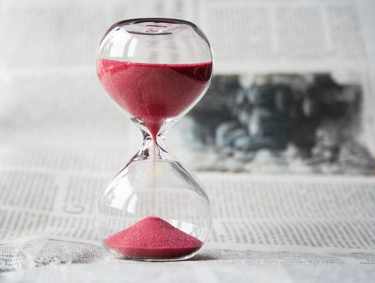 An image of an hourglass with pink sand placed on top of a newspaper. Learning the Portuguese alphabet takes time.
