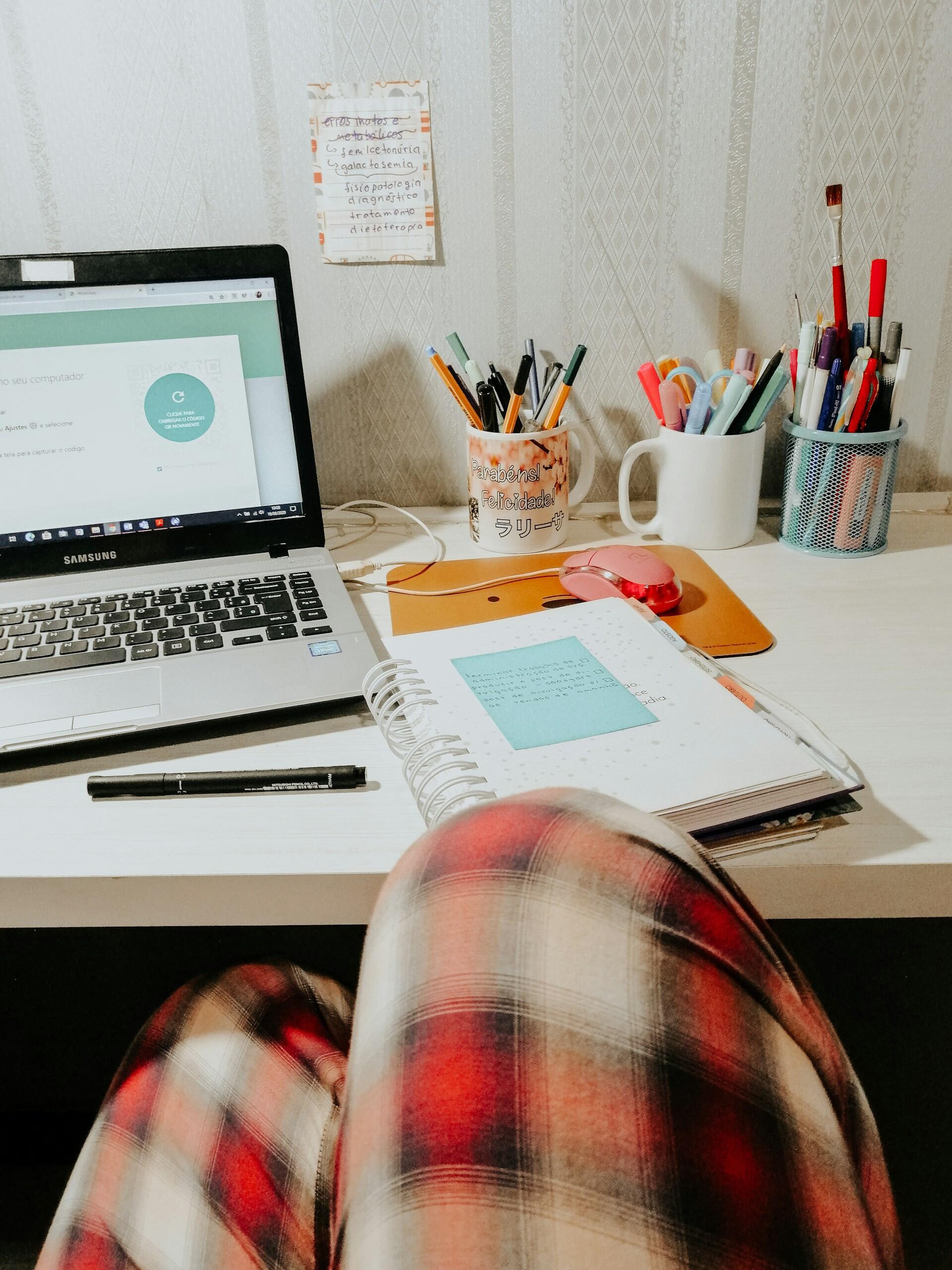 A person sitting at a desk with an open computer and a notepad. 