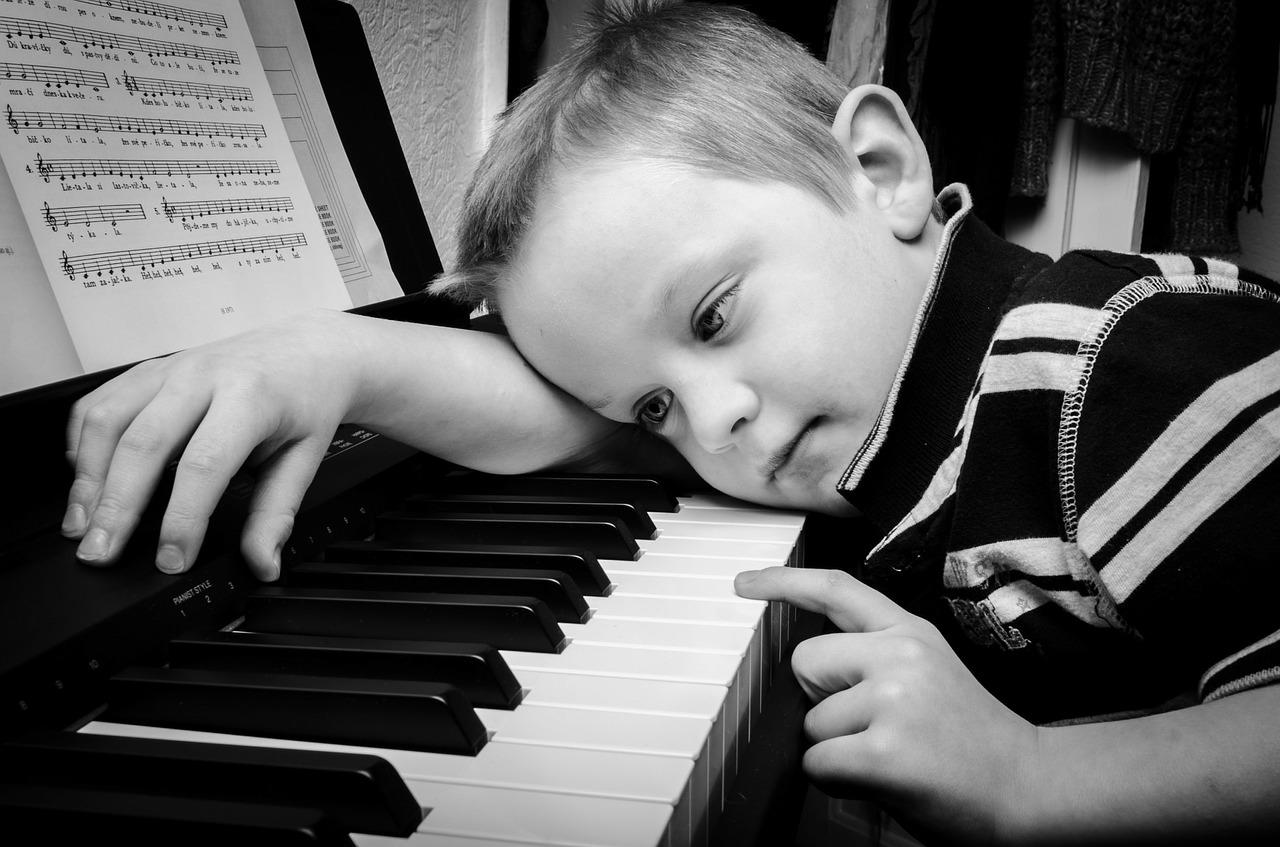 A boy falls asleep on a piano