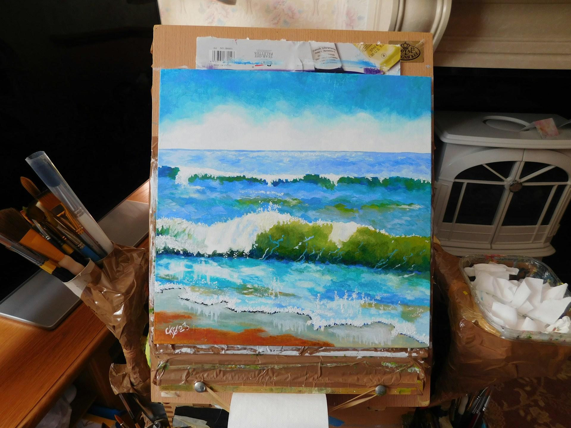 canvas of a coastal landscape surrounded by paints and art supplies