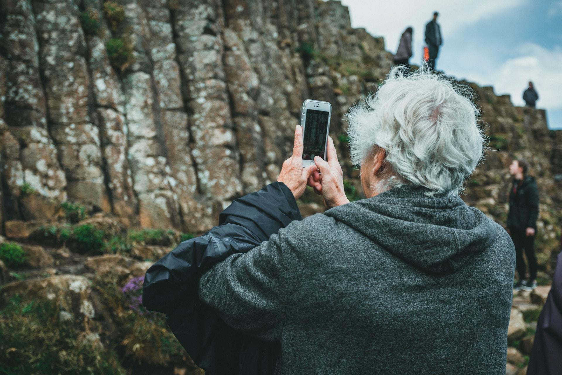 A senior with white hair is taking a picture with his mobile phone.