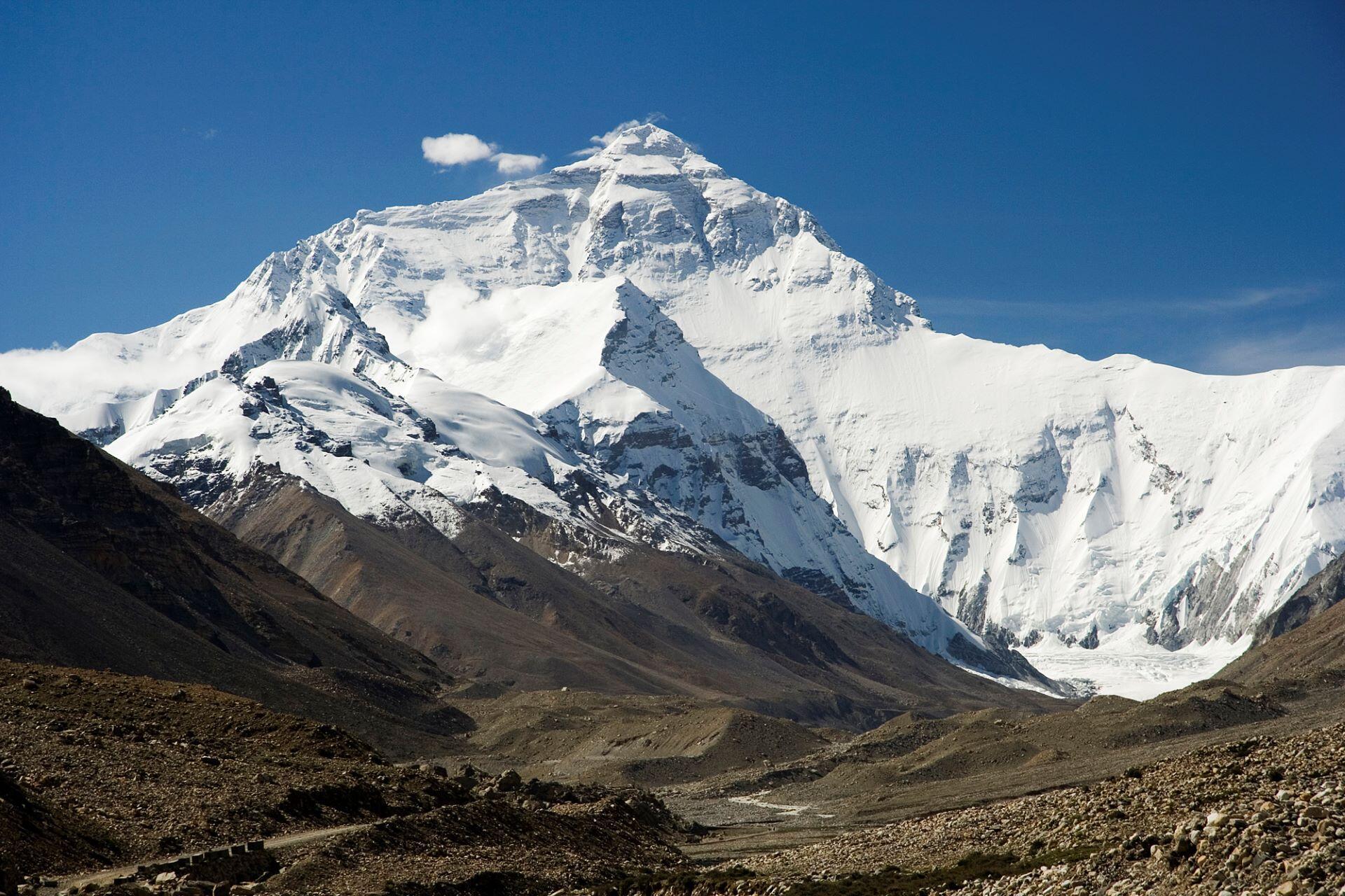 Snow-covered Mount Everest rising above rocky terrain under a clear blue sky.