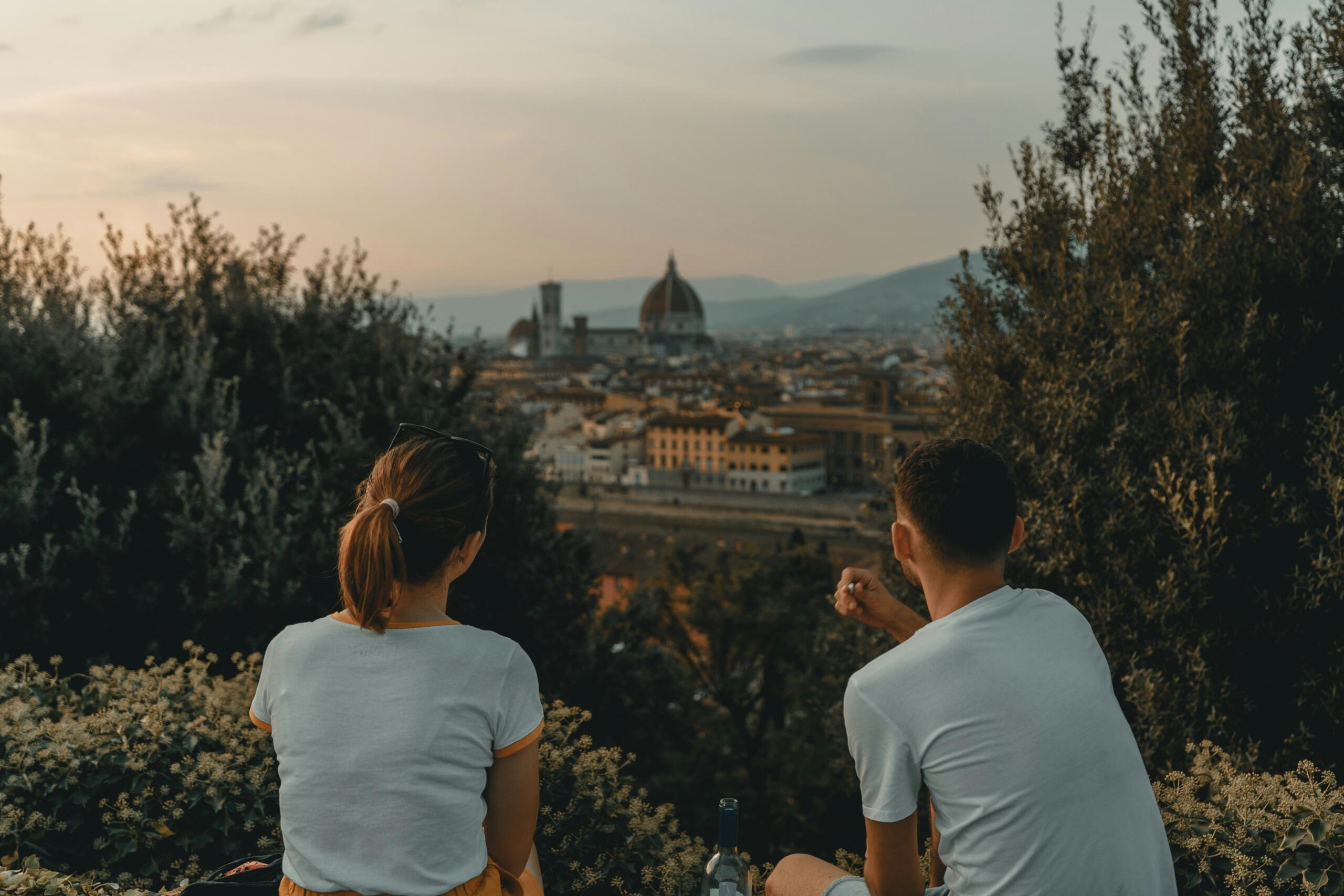 A couple enjoys a sunset view over Florence, with the iconic cathedral in the background, surrounded by greenery.