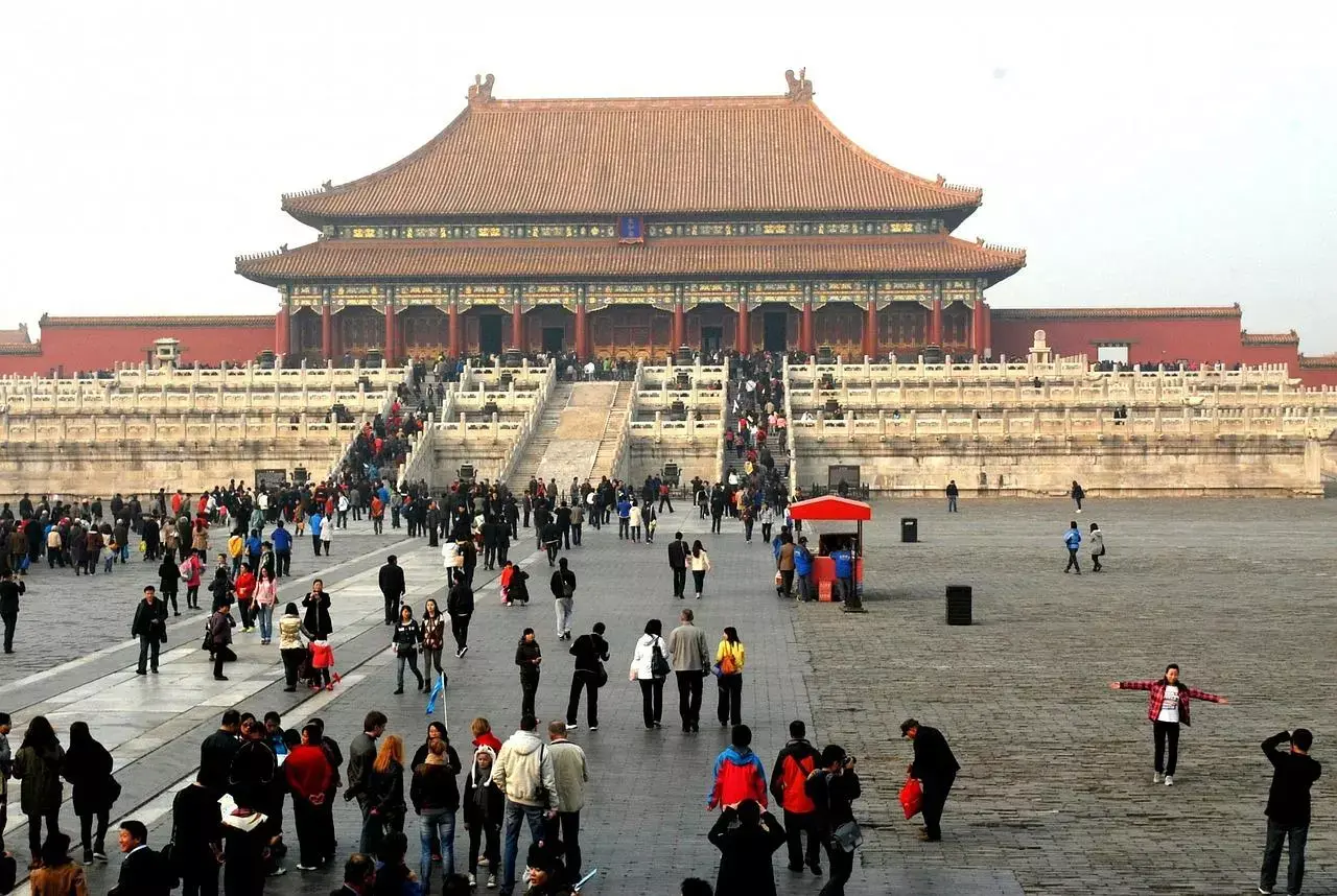A large structure behind a great plaza with people milling about.