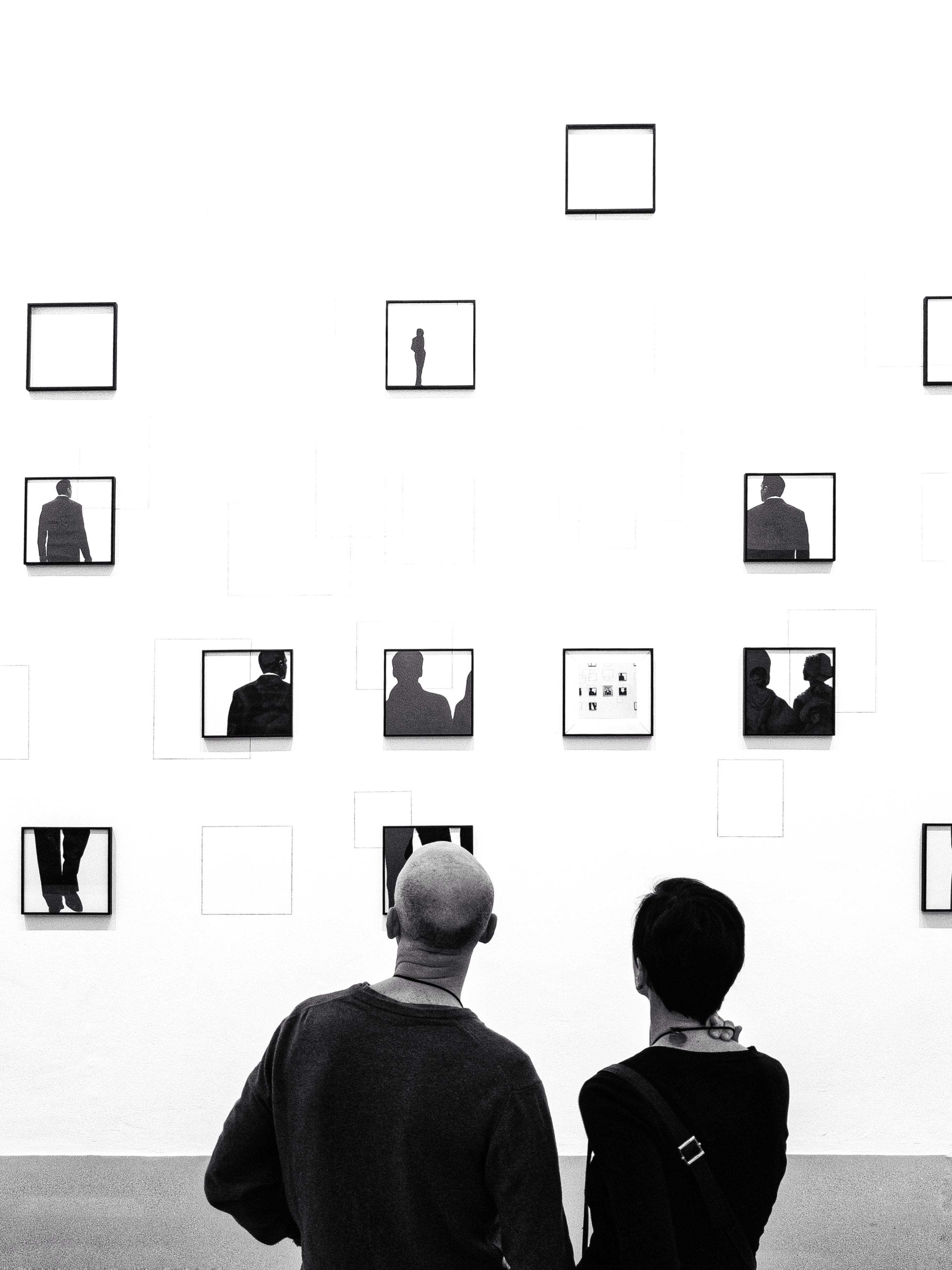 Two people look at paintings in an exhibition