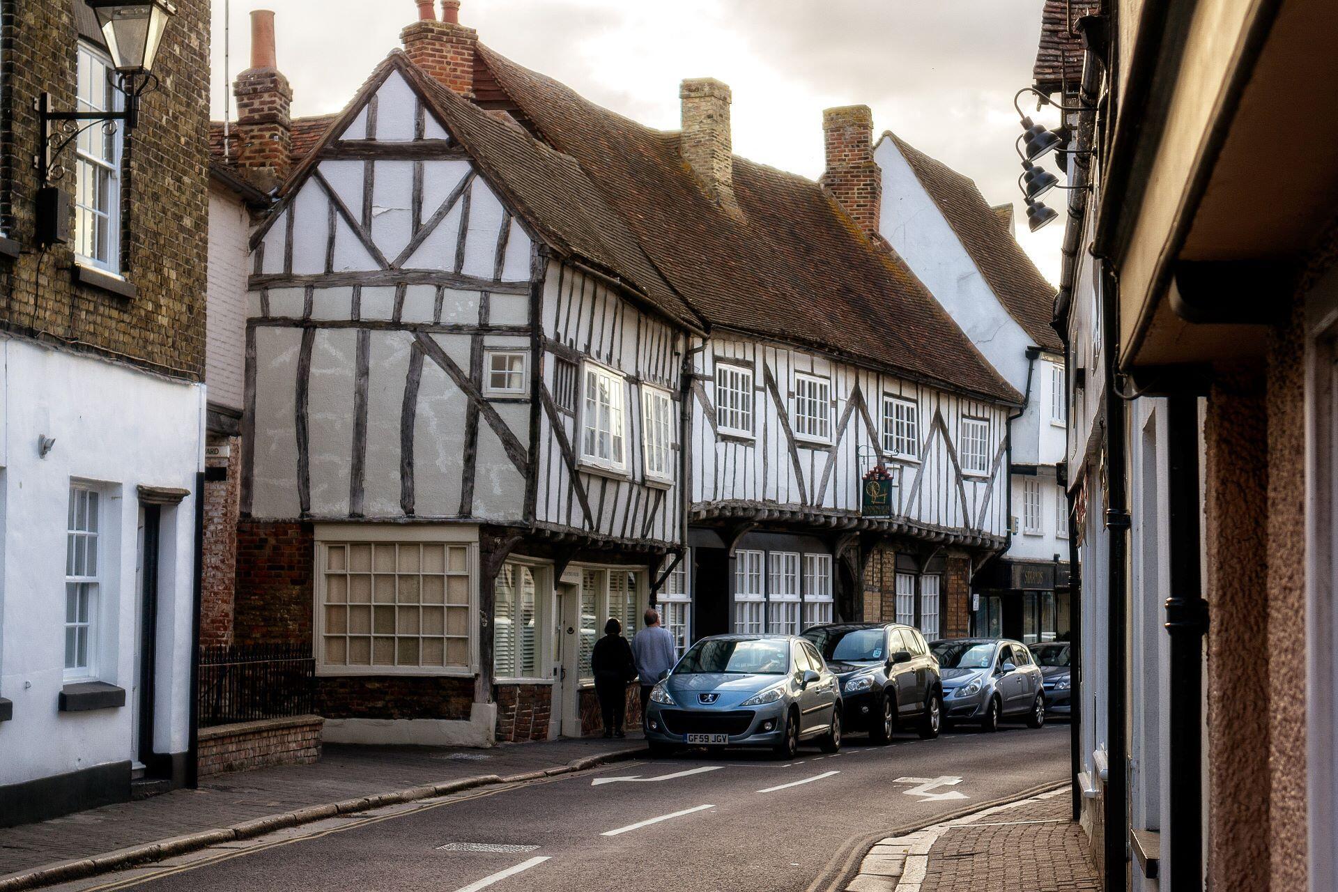 Timber-framed Tudor houses with white plaster walls, dark wooden beams, and steep tiled roofs along a narrow street.