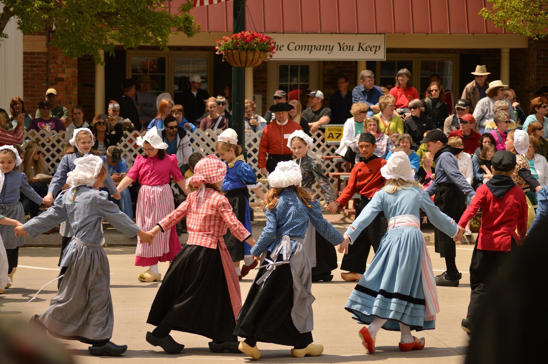 Kids dancing around in a circle holding hands while the adults watch. Some dance classes for kids may be commissioned to set up big performances for annual cultural events or government-sanctioned celebrations