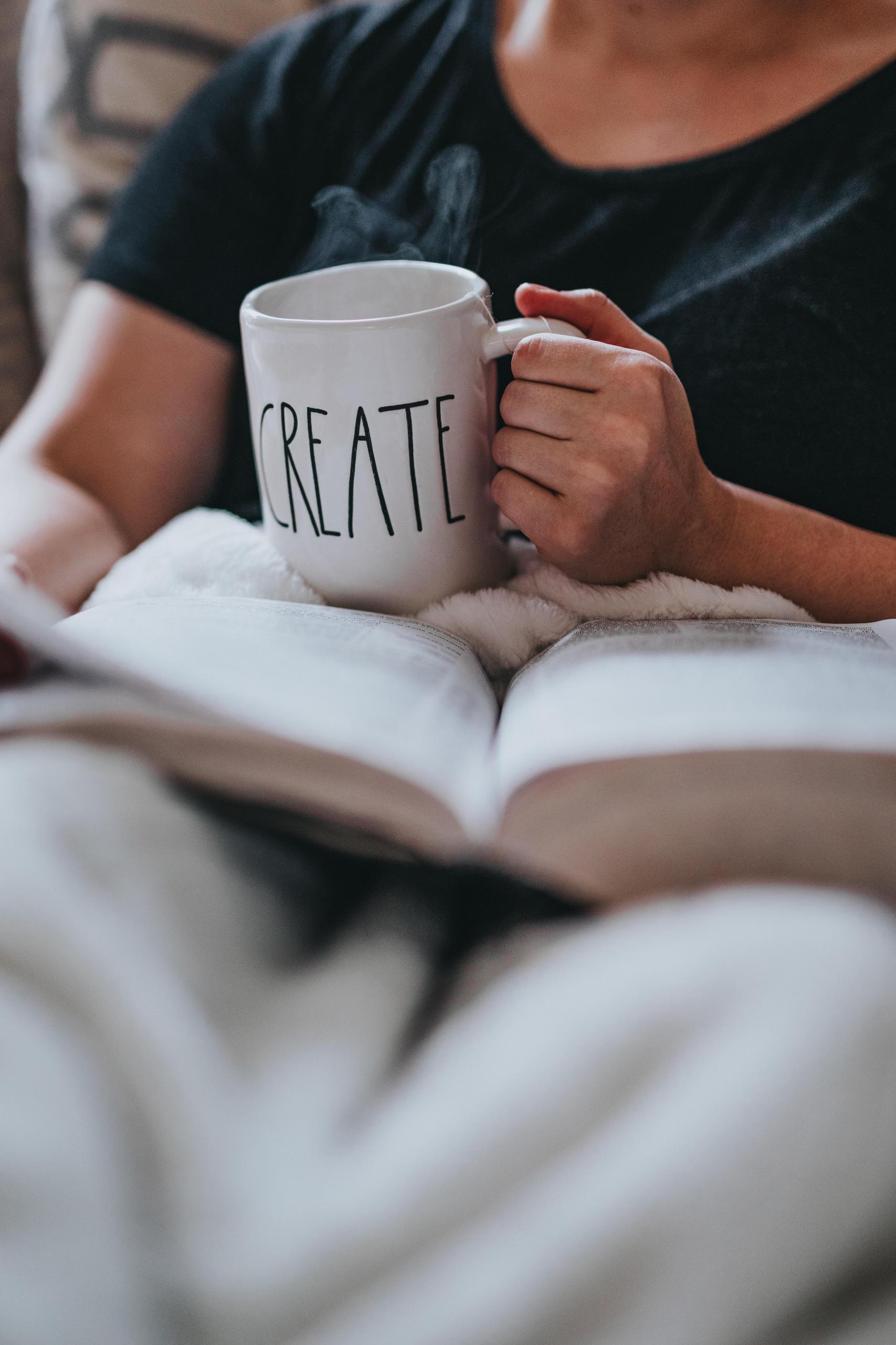 A woman reading a book with a mug of coffee in hand.