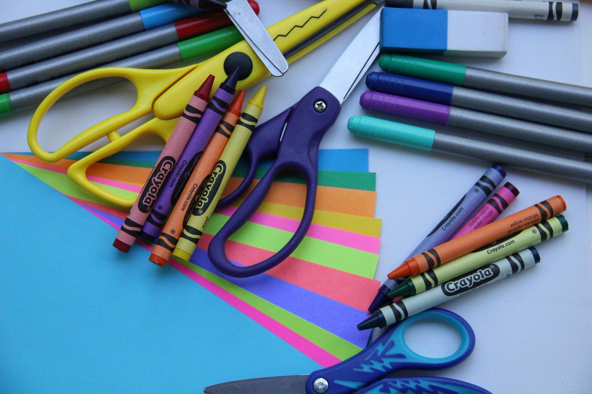 A colourful assortment of school supplies, including scissors, art paper, coloured pencils and felt-top markers.