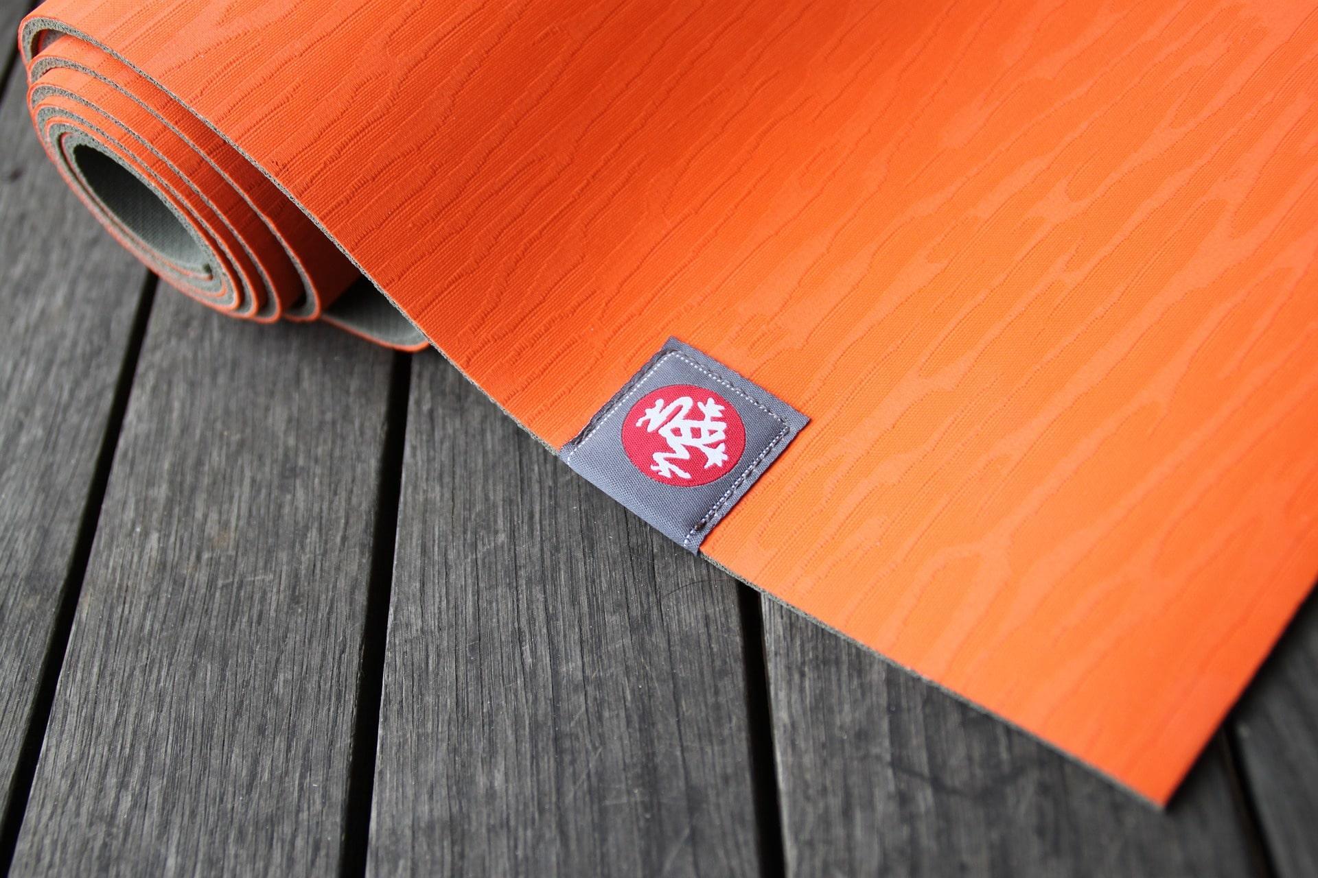 An orange yoga mat partially rolled up, laying on a wood-planked surface.