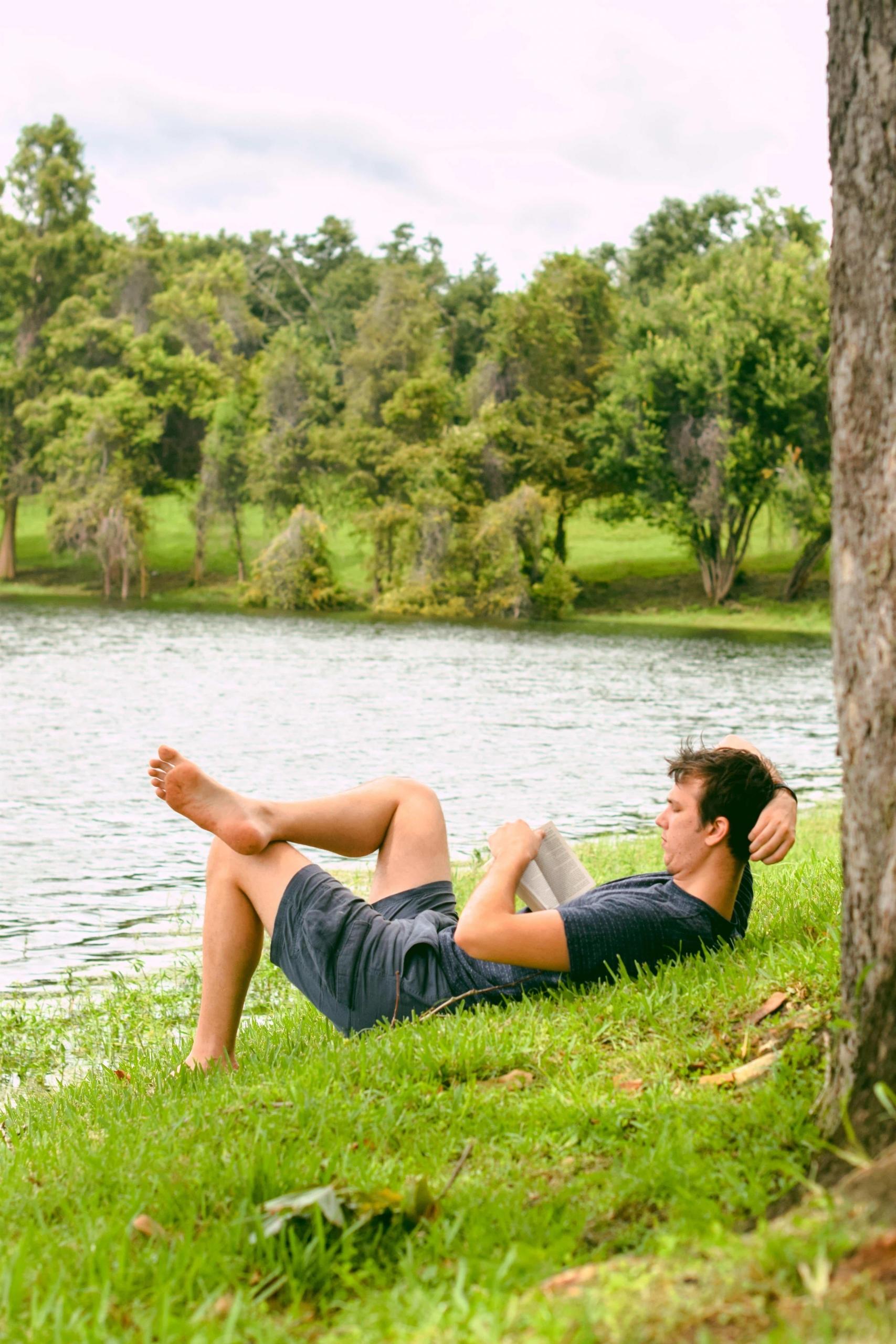 Man laying on river bank reading