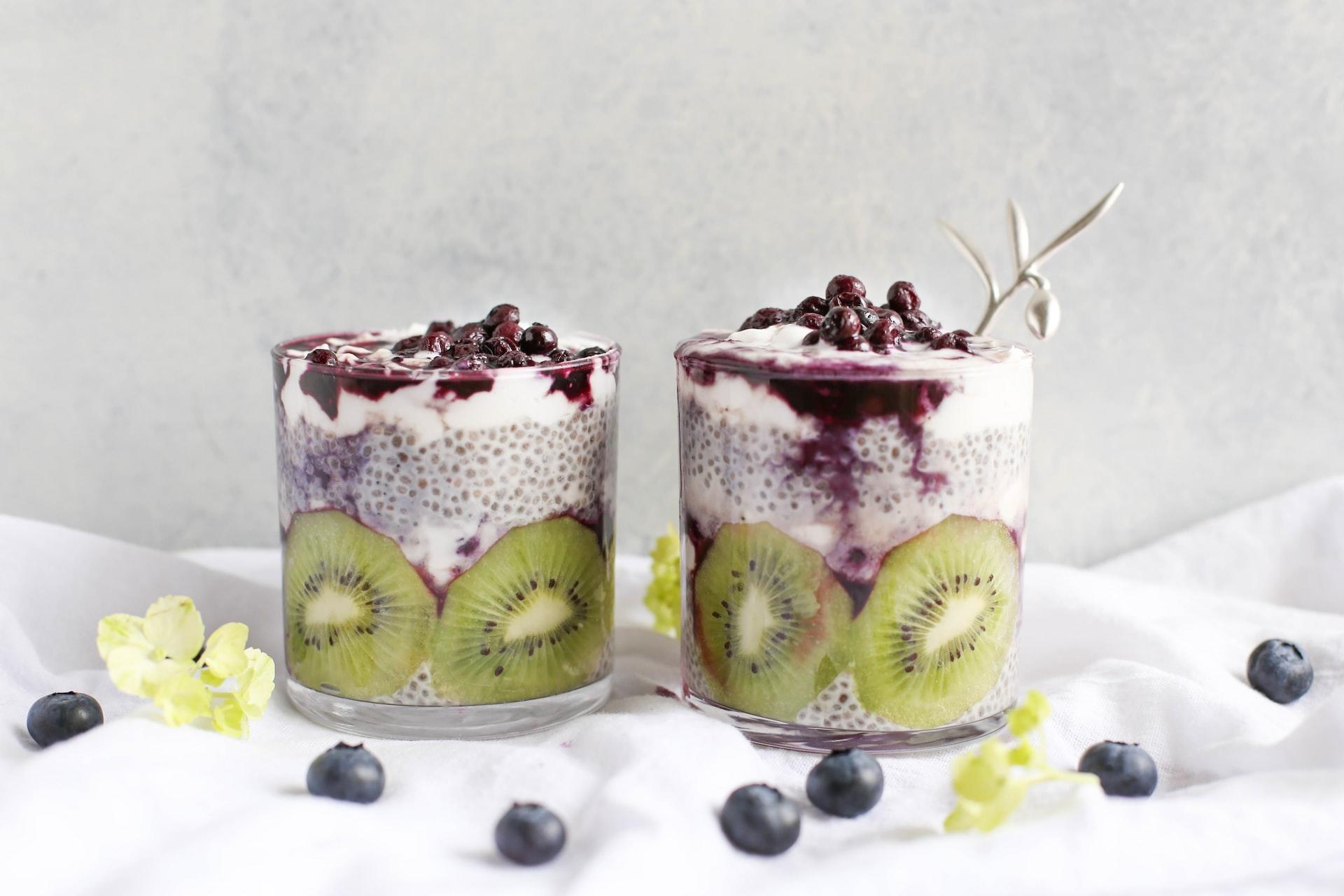 Two clear glasses containing kiwi slices and chia seed pudding topped with blueberries