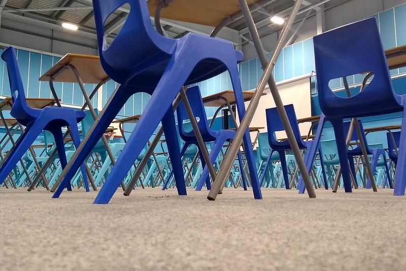 A testing centre with blue walls, outfitted with dark blue chairs and foldable desks, set up and ready for test-takers. 