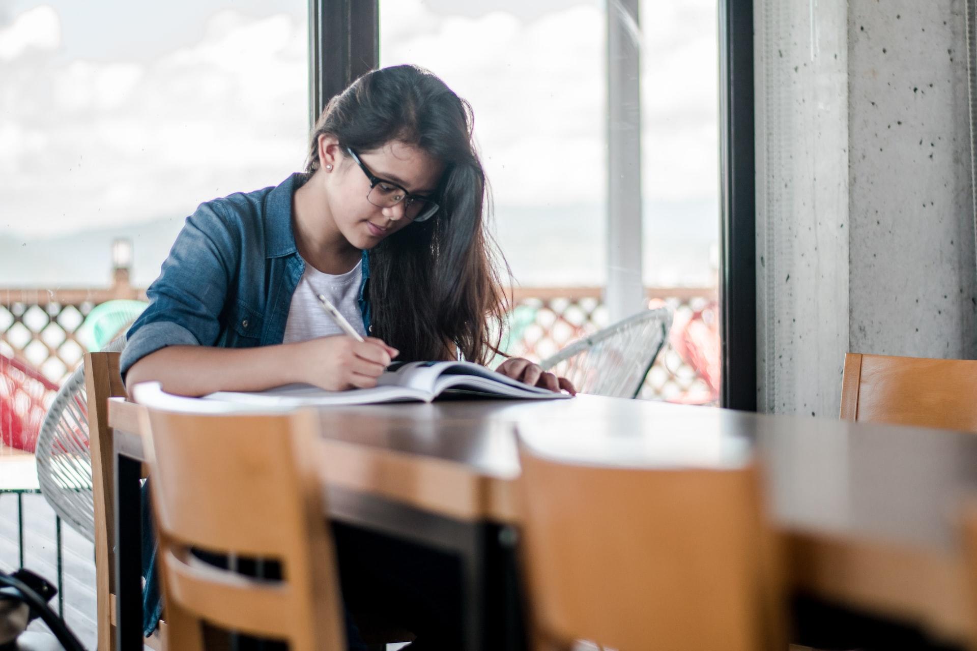 A woman with long hair and glasses sitting at a table, studying