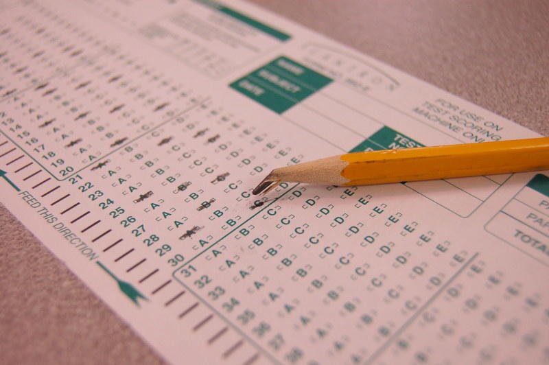 A bubble test answer strip printed in green ink, with a few answers marked out in pencil and a yellow pencil with a broken lead laying on the sheet. 