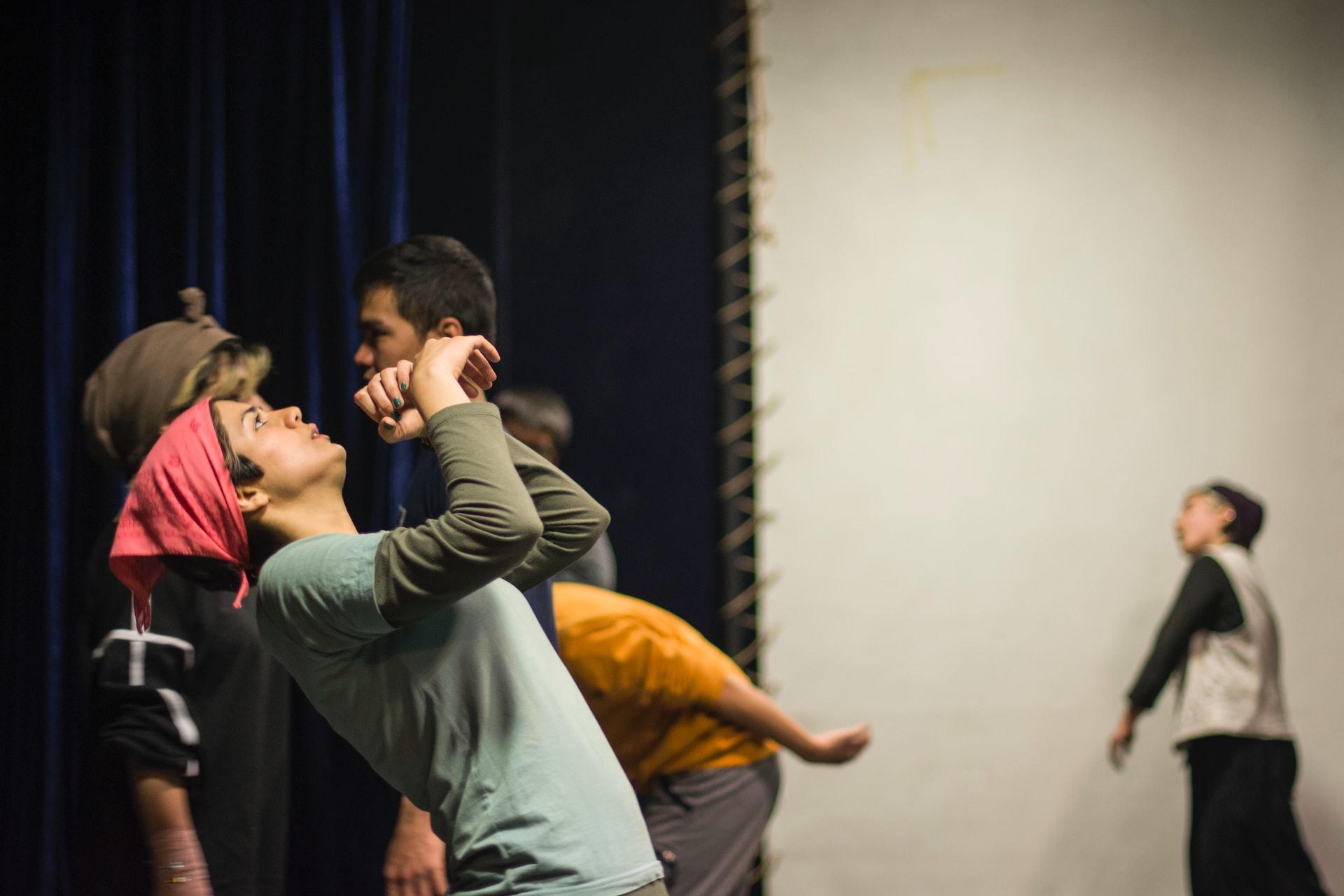 A student wearing a red headscarf and dark jumper looks skyward while another student in the background moves about jerkily