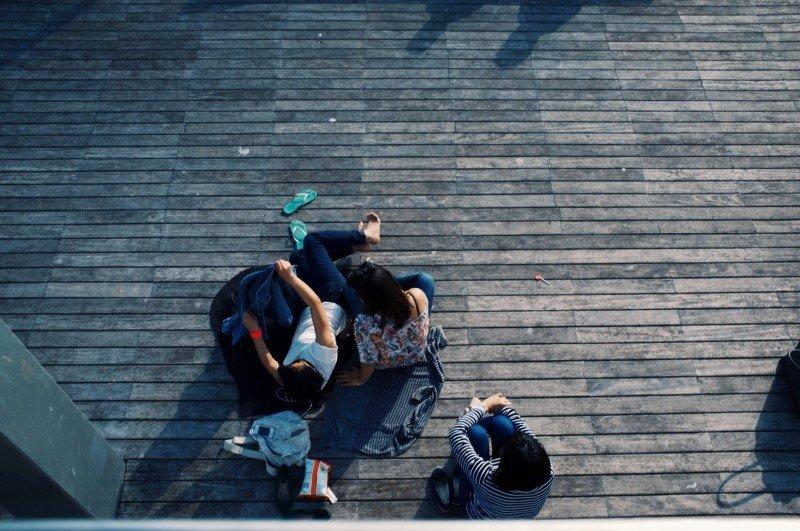 An overhead shot of three people arranged in various positions on wood plank decking at sunset. 