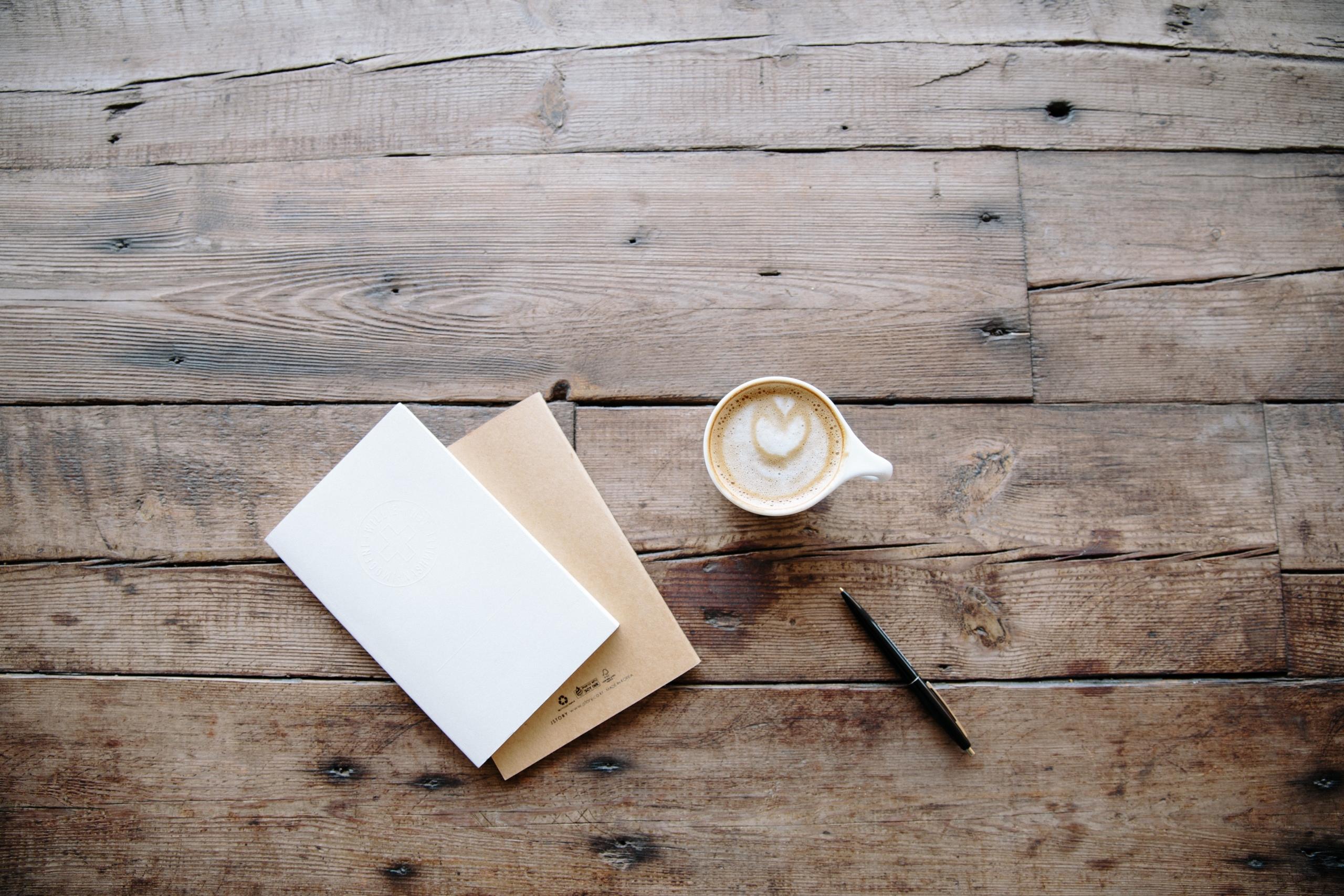 Wooden table with coffee, notebooks, and a pen