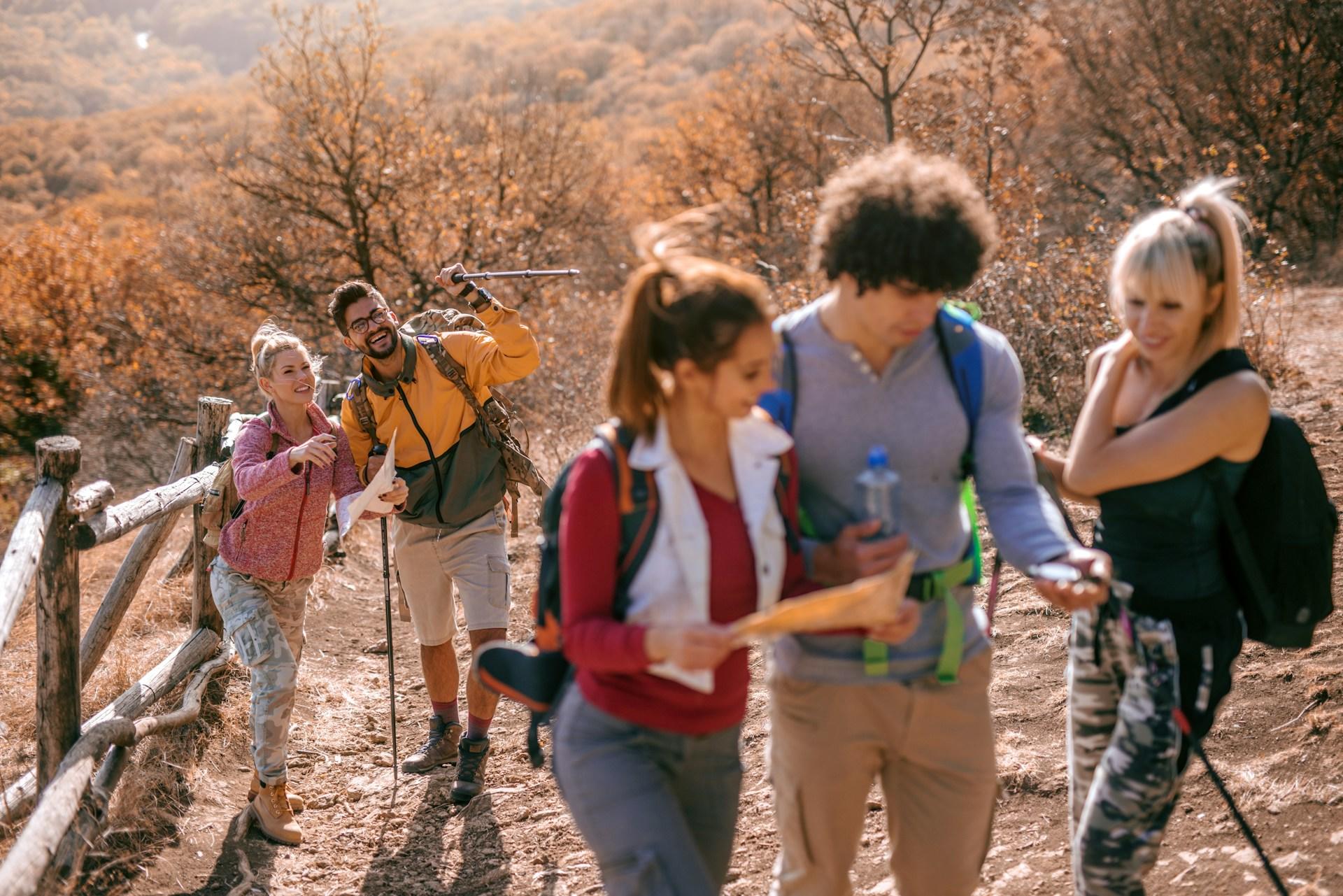 A group of hikers with Nordic walking poles stops on an uphill with a backdrop of brown scrub to consult a compass.