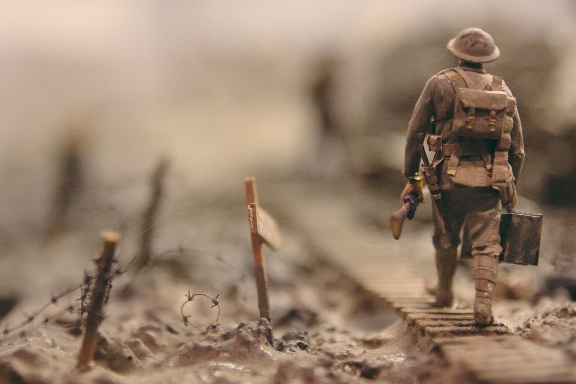 A soldier in full khaki combat dress carrying a rifle and munitions kit walking on train tracks next to strung out barbed wire