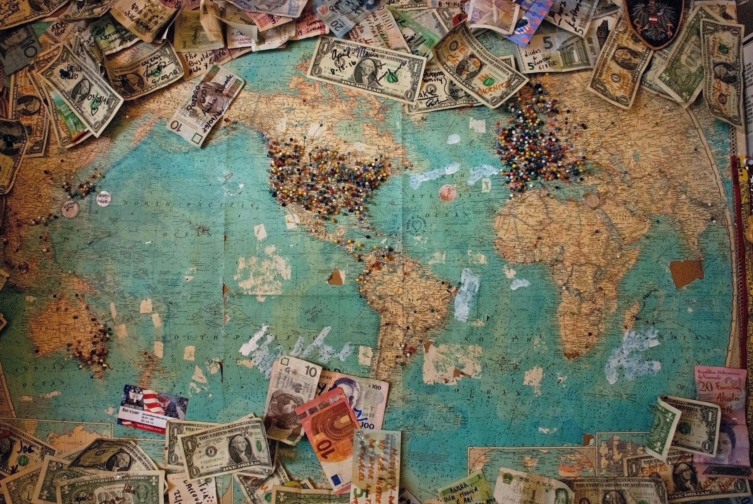 A picture of the world map with the Americas centered and pins marking the major population concentrations, ringed with paper money in various currencies including USD, Euro and GBP