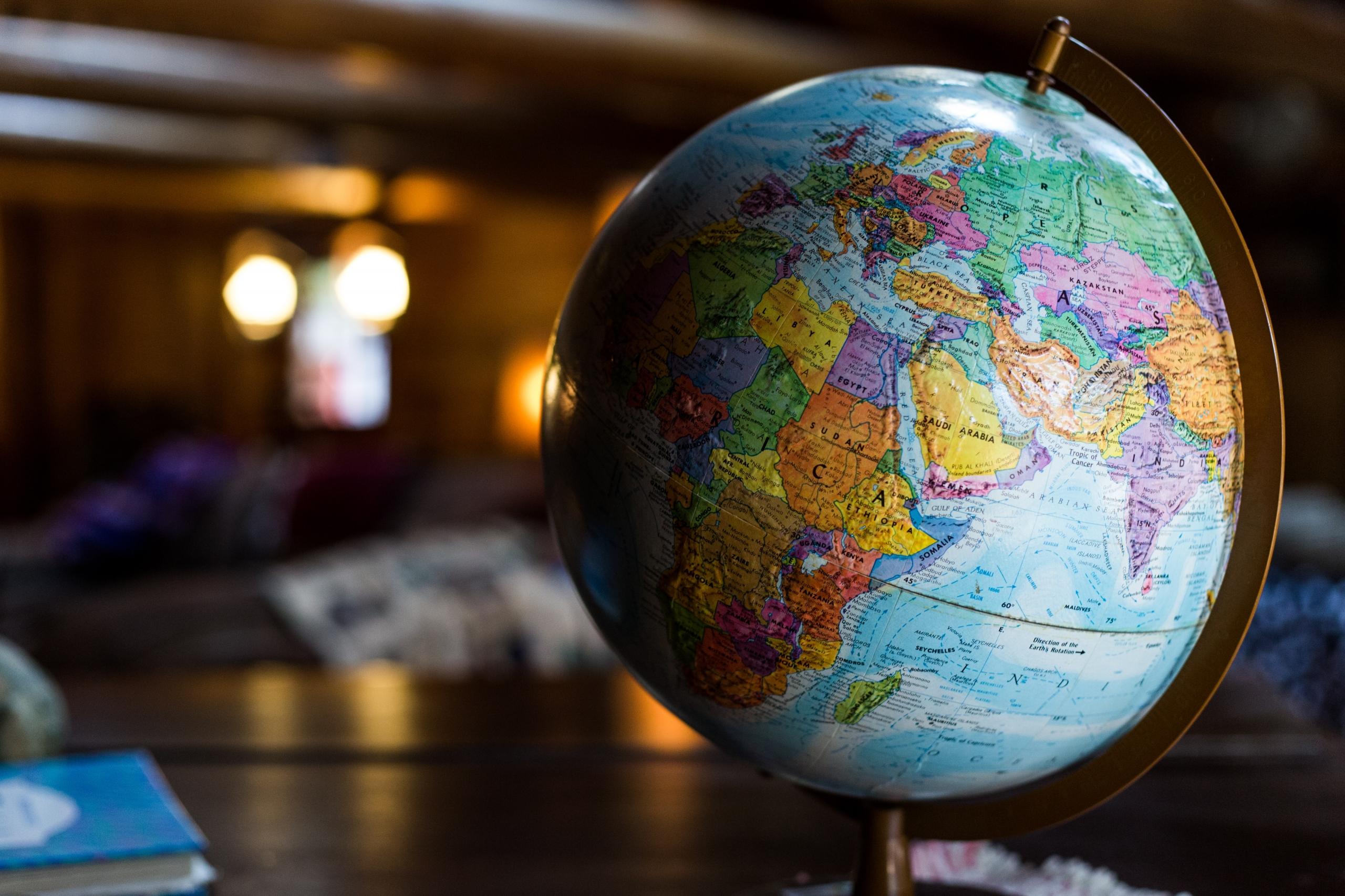 A desk globe sits on a surface in a darkened room that has mellow light far in the background.