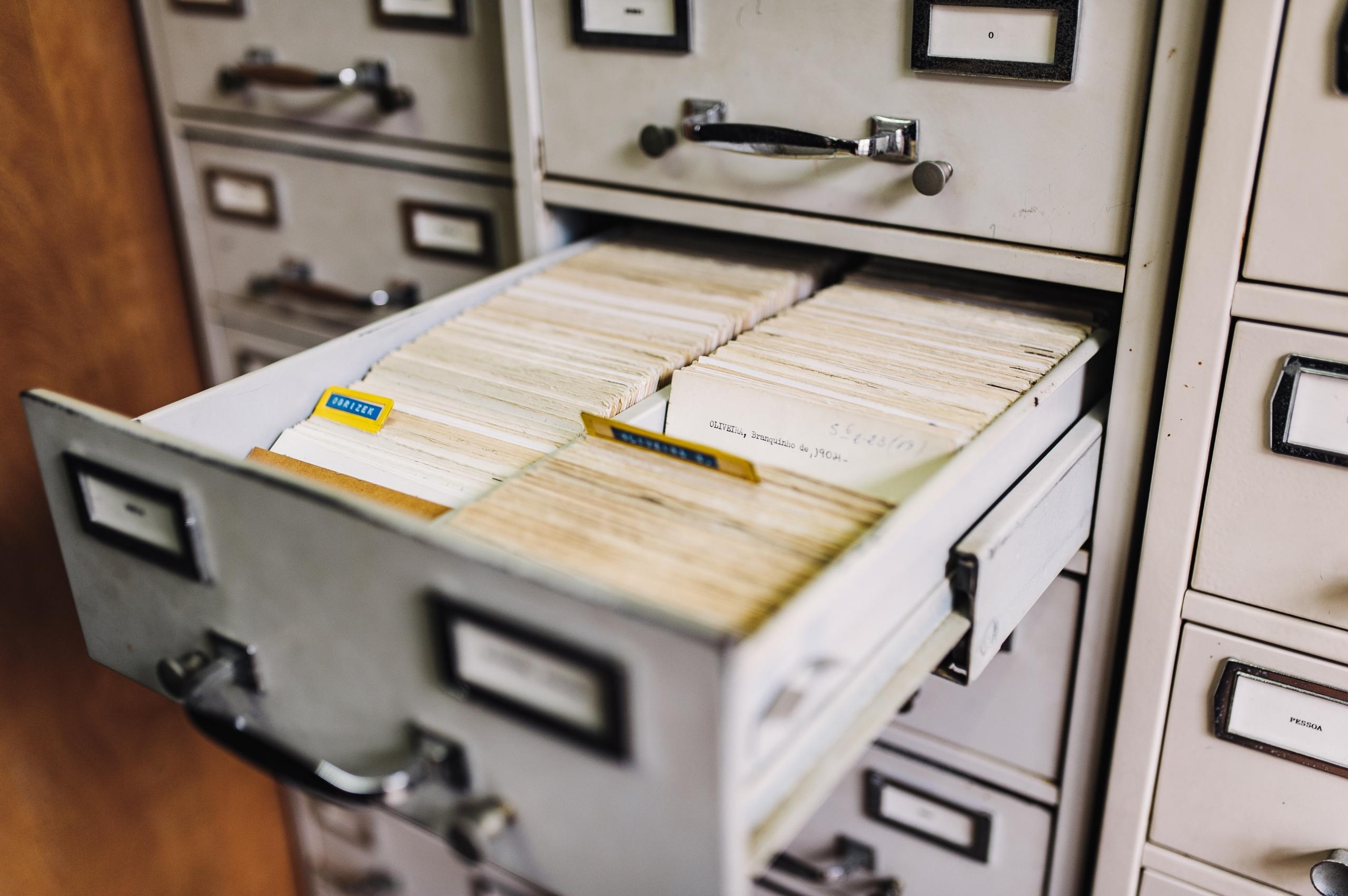 a grey library card catalogue file with one drawer open to reveal index cards