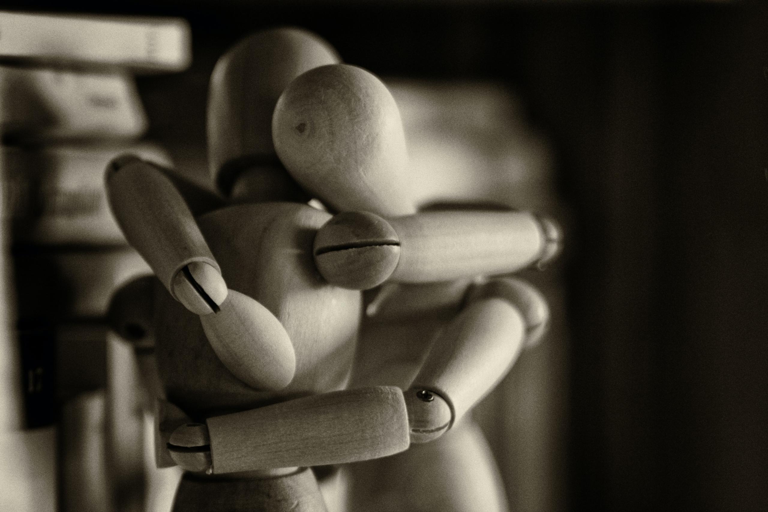 A greyscale image of two wooden art dolls posed in a hugging position.
