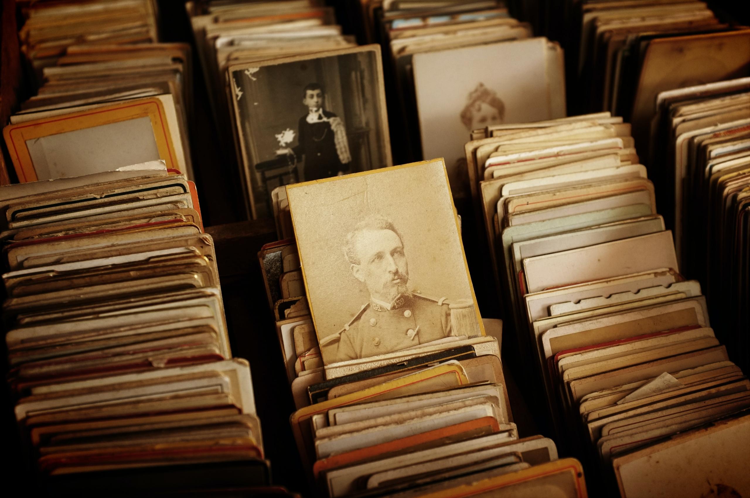 A collection of old photos organised into racks like vinyl records, with one sepia-toned image showing a man in military uniform and two more, in the background, showing a boy dressed in black and a woman wearing a hat, respectively. 