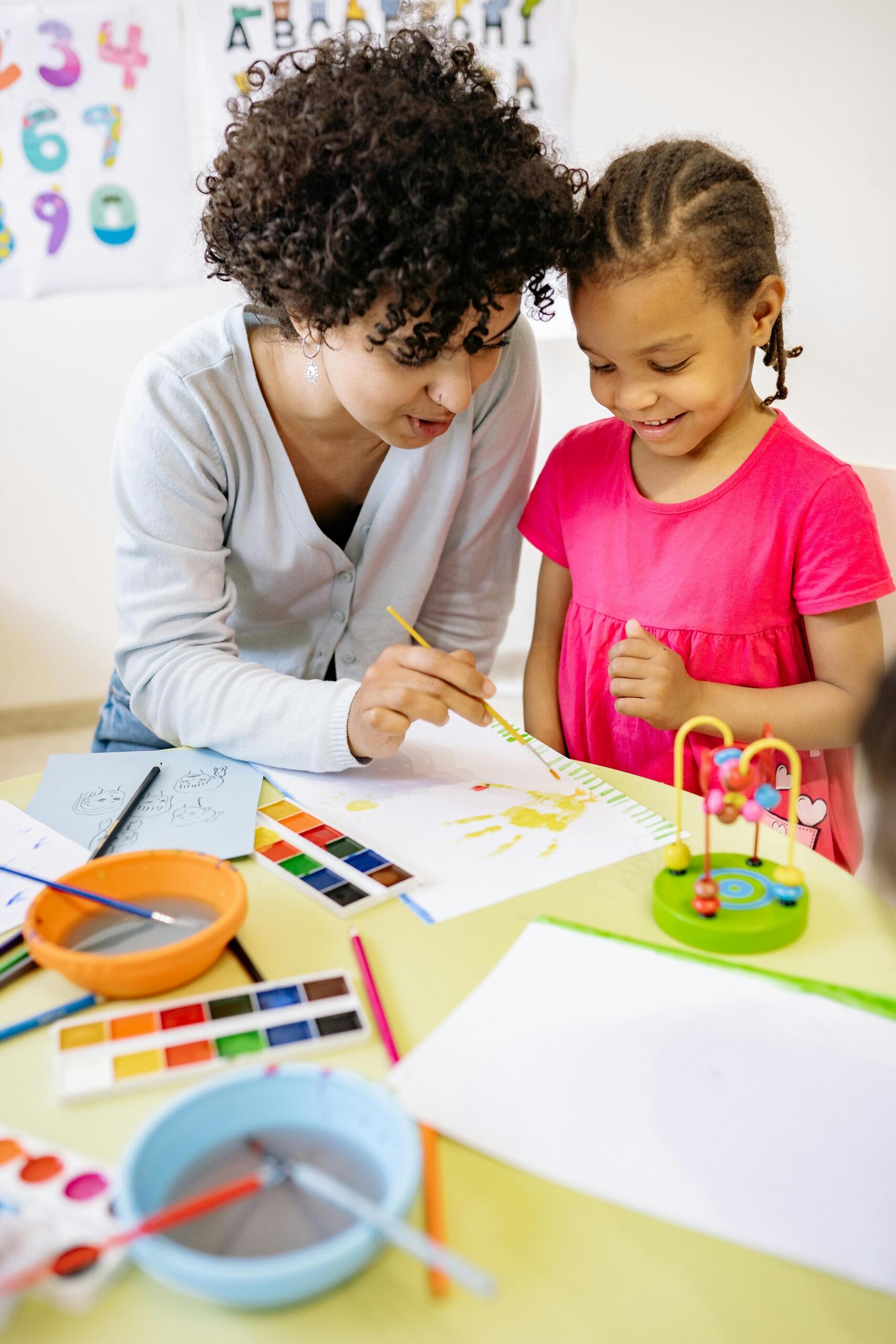 Woman teaching a girl in pink dress to paint