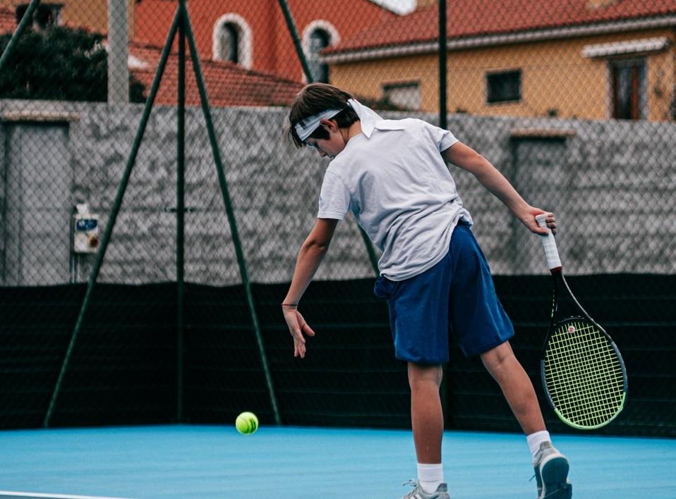 A young tennis player bouncing the ball while practicing his serve