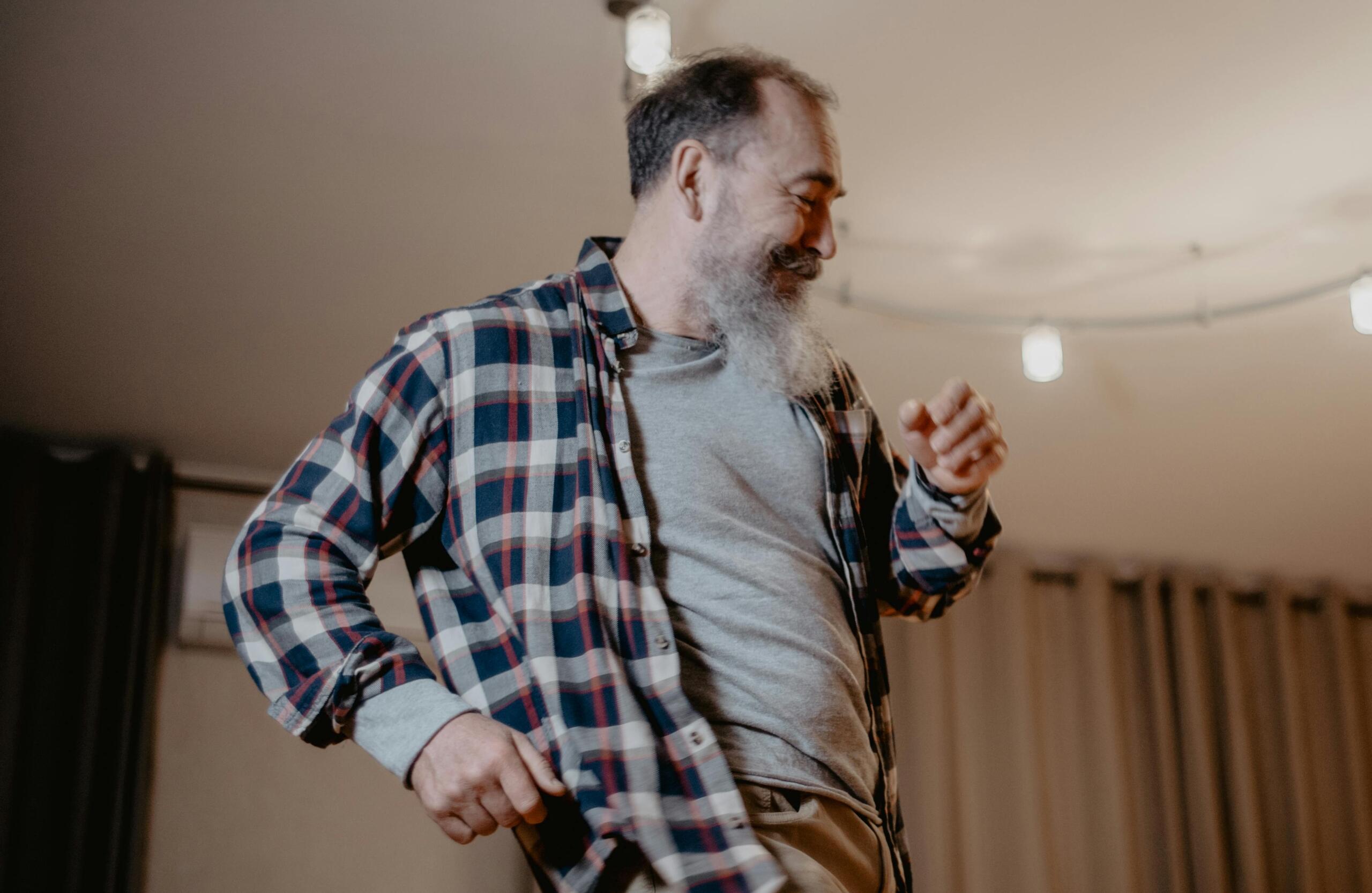 An elderly man dancing indoors with joy and confidence.