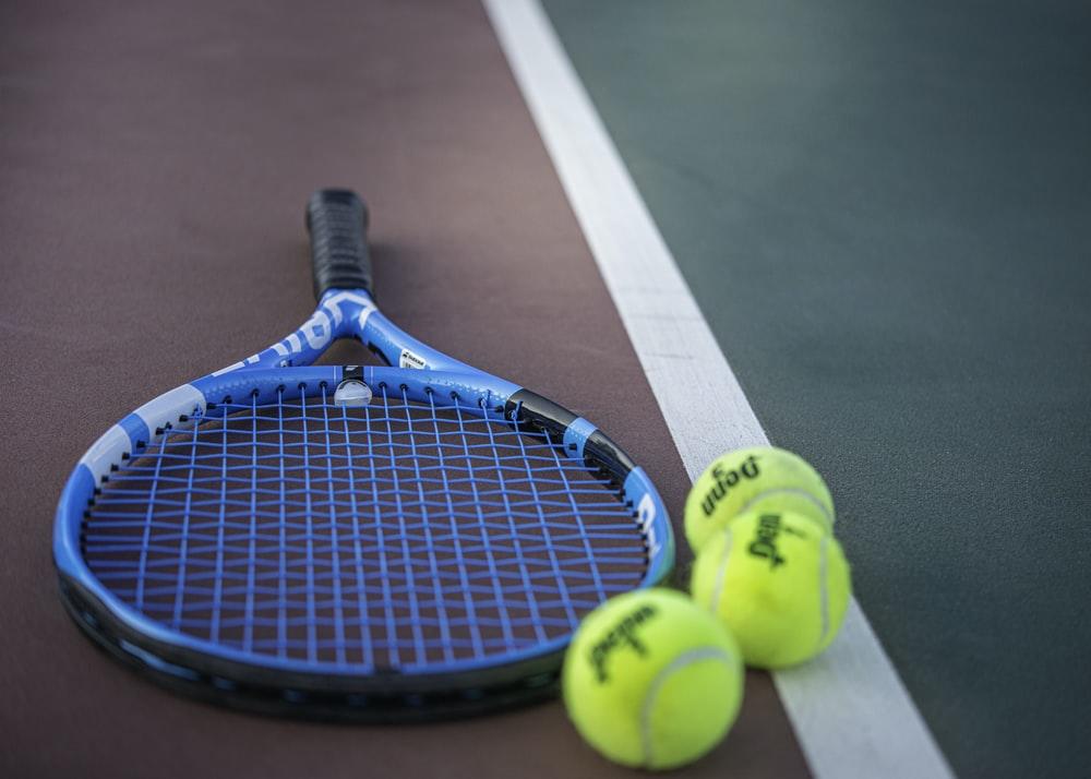 A racket laying on the tennis court along with three tennis balls