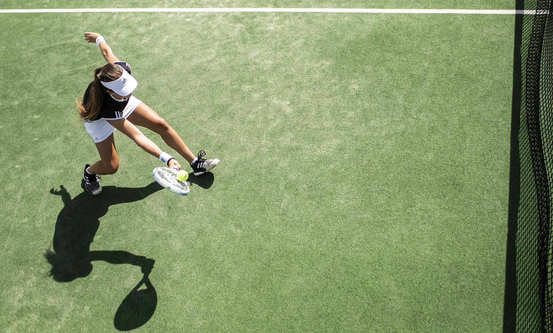 A girl serving the tennis ball on a grass court