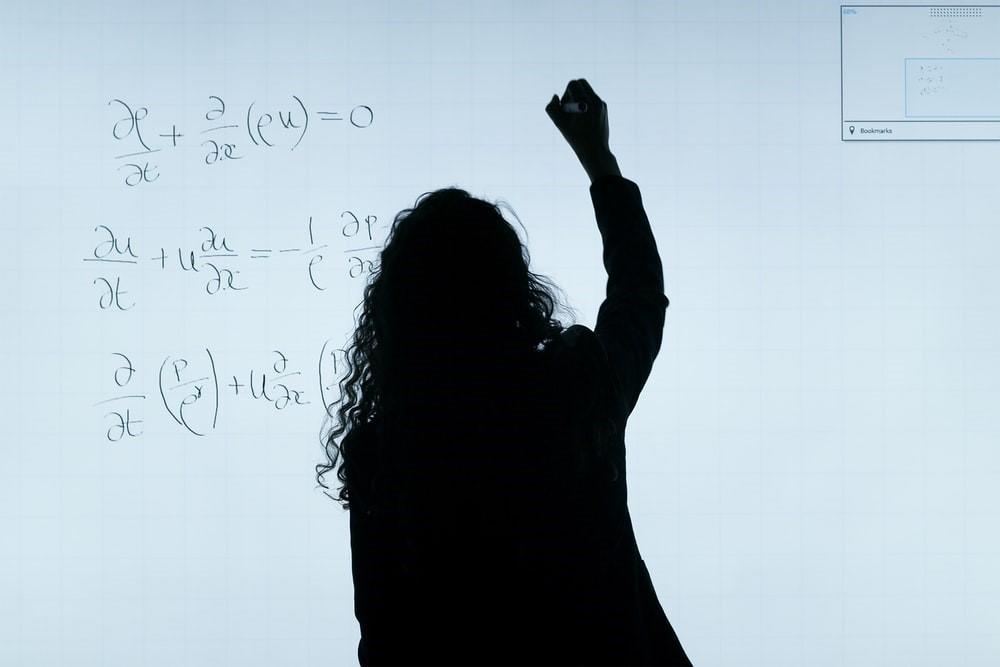 A lady writing algebraic equations on a whiteboard