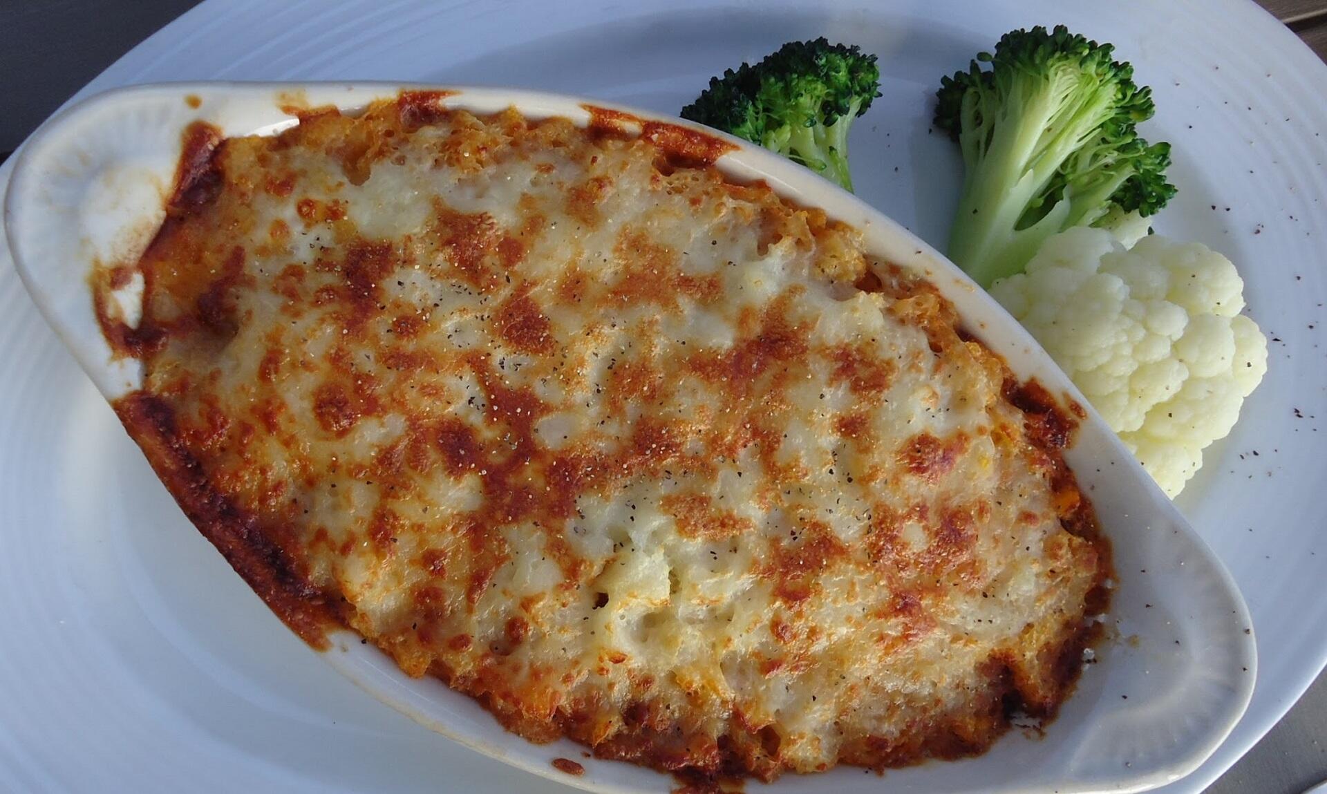 An oval dish presenting a baked food, served with broccoli and cauliflower.