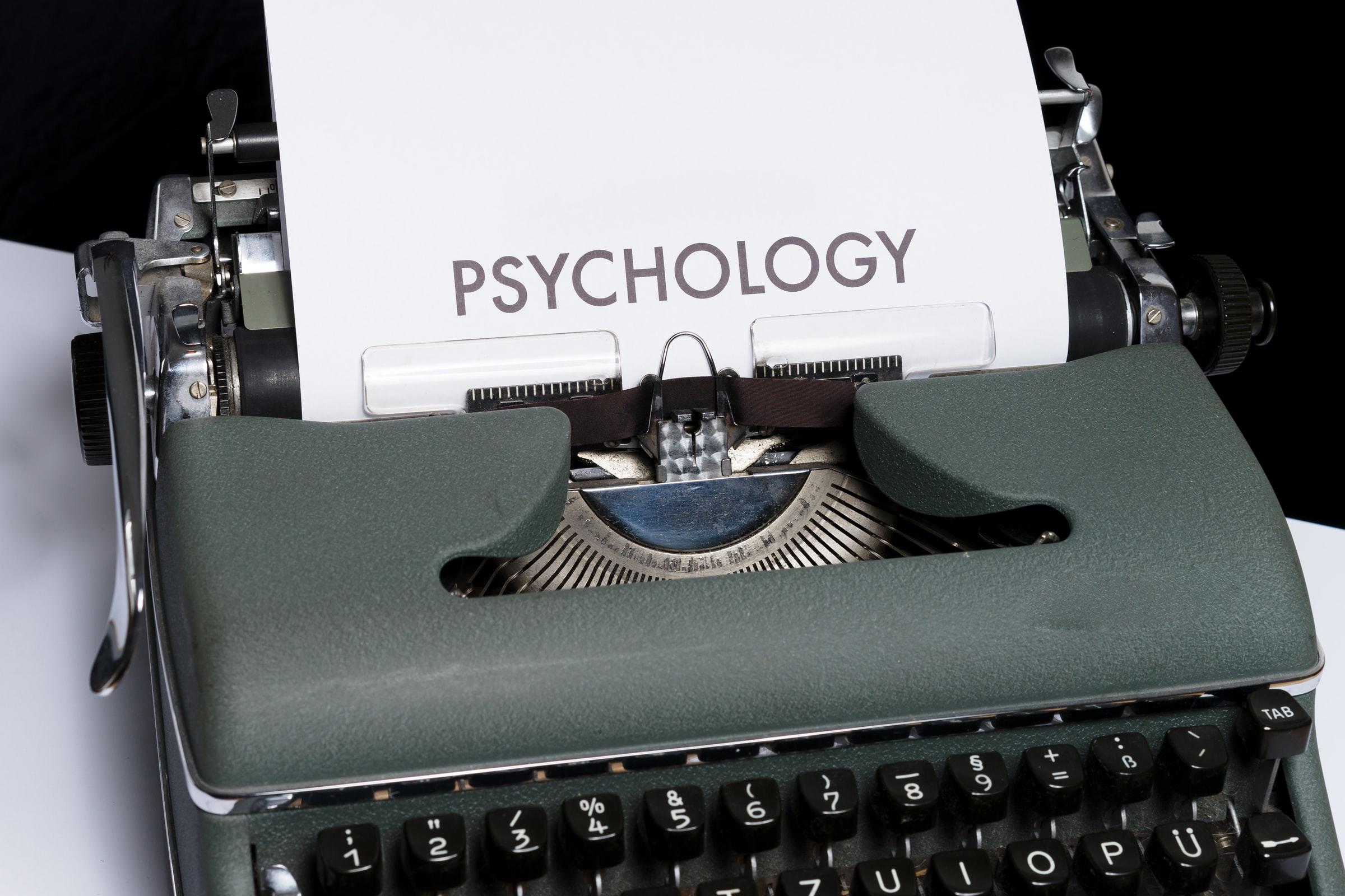 A grey typewriter with black keys displays a page with the word psychology written on it in capital letters.
