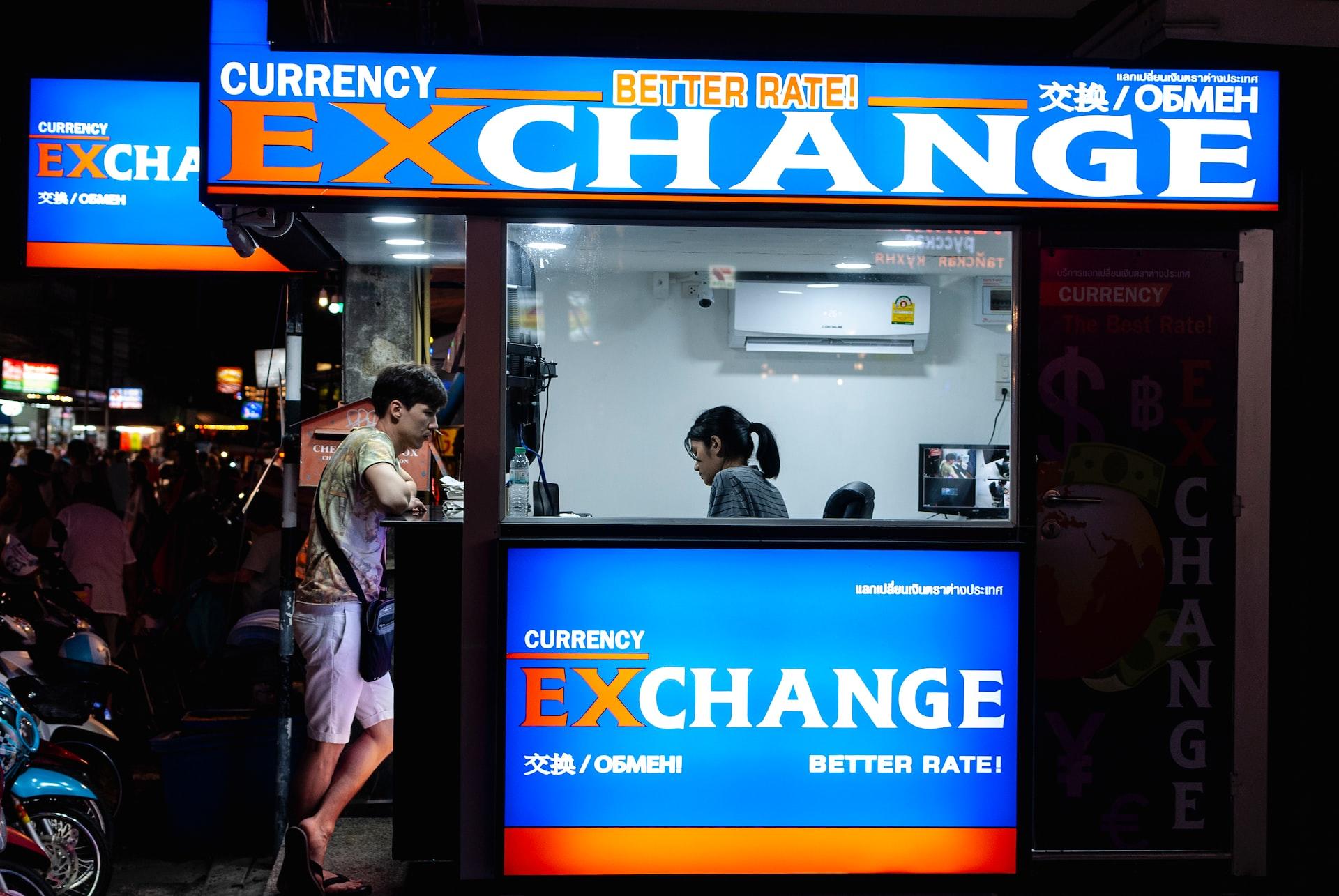 A customer at a blue neon-lit currency exchange booth at night. 