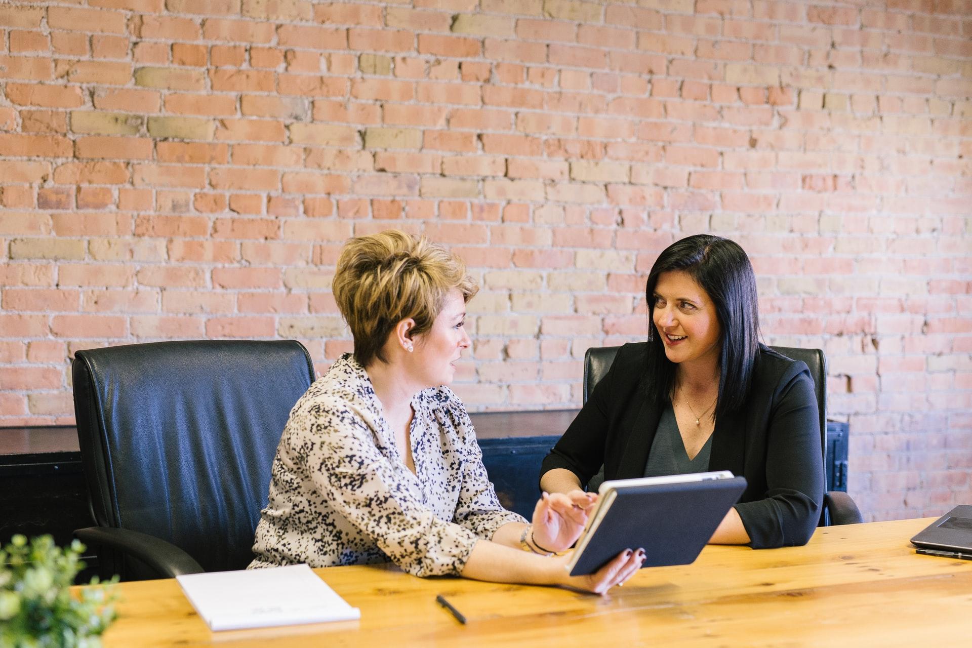 Two women sitting at a wooden table with a brick wall behind them