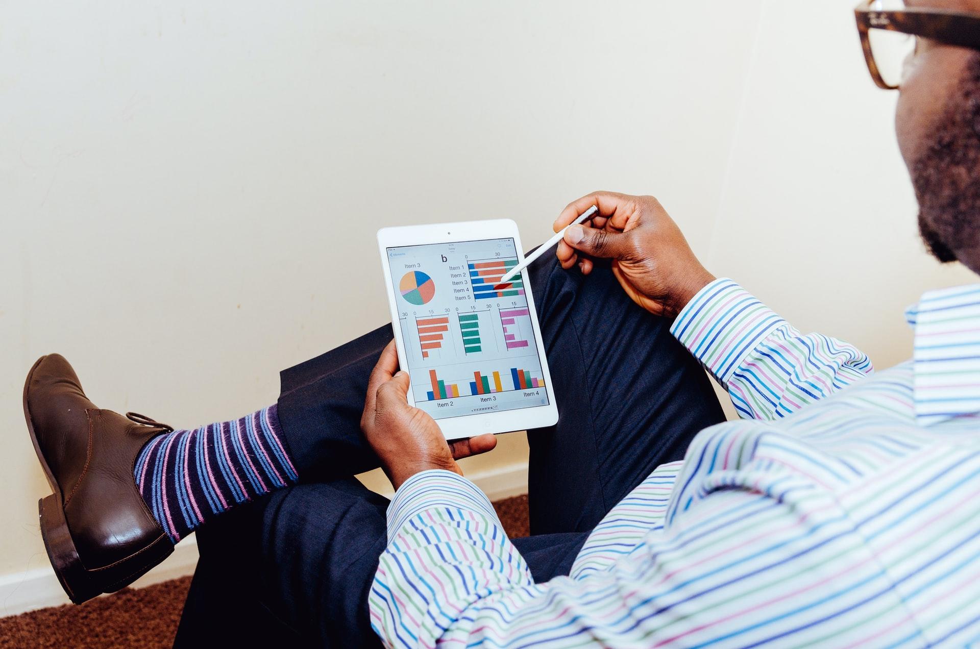 A man in a blue shirt and dark slacks holding a computer tablet displaying various graphs