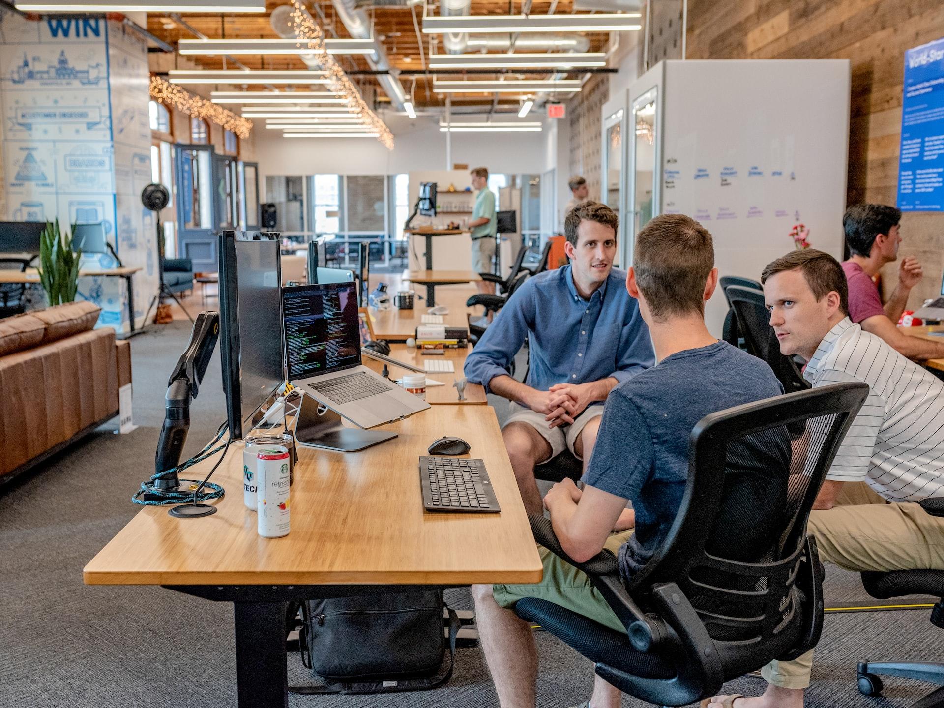 Three men sitting in a brightly lit office discussing something