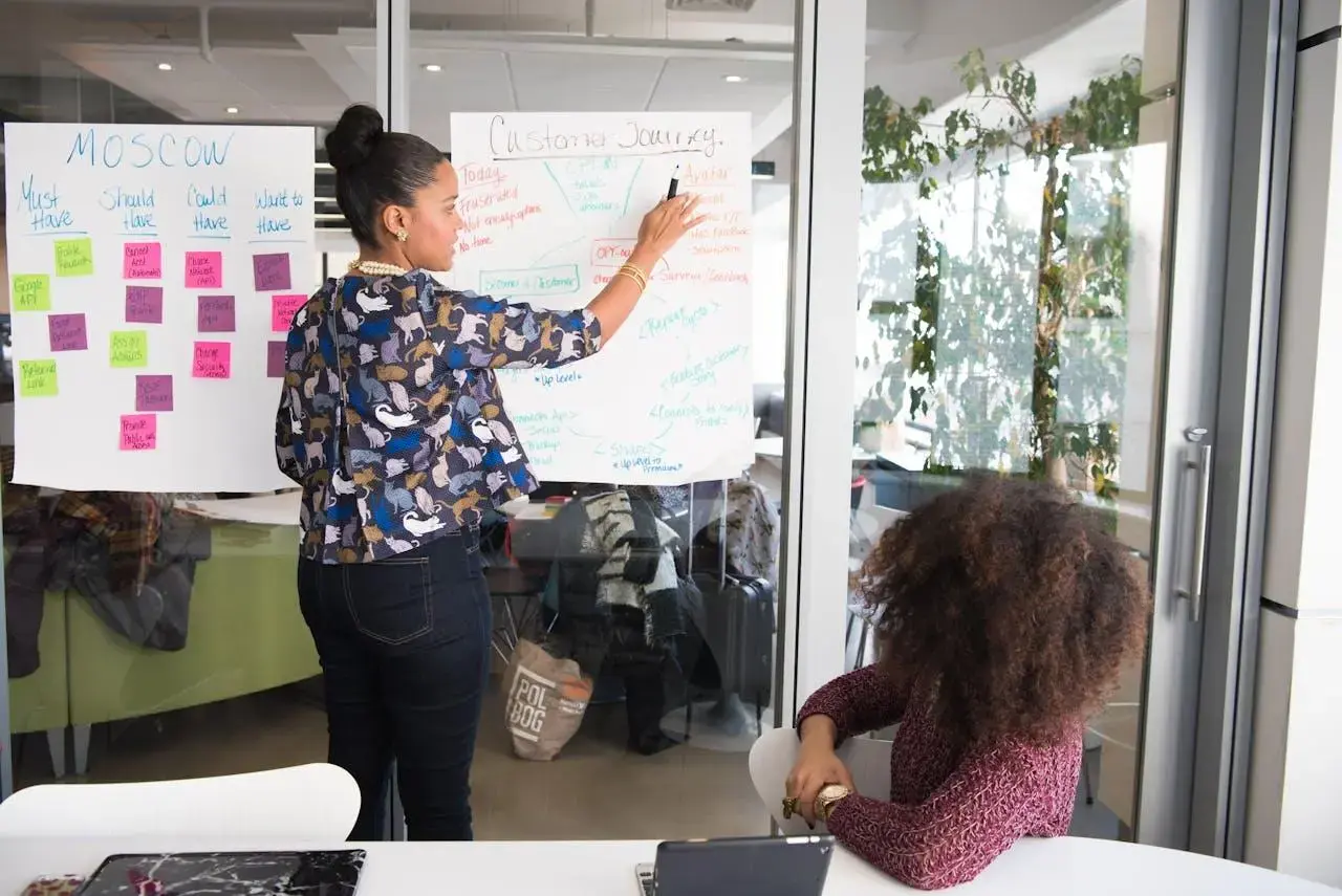 woman standing in front of a whiteboard presenting to a student