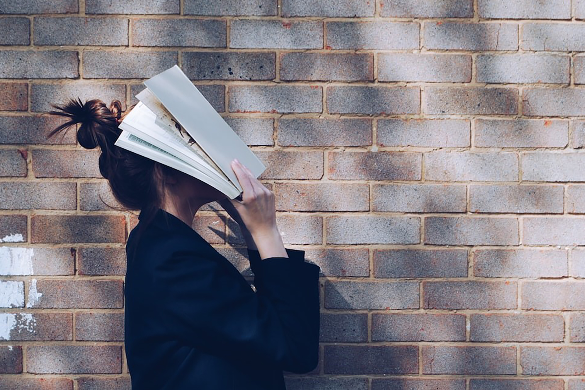 A girl covering her face with a book.